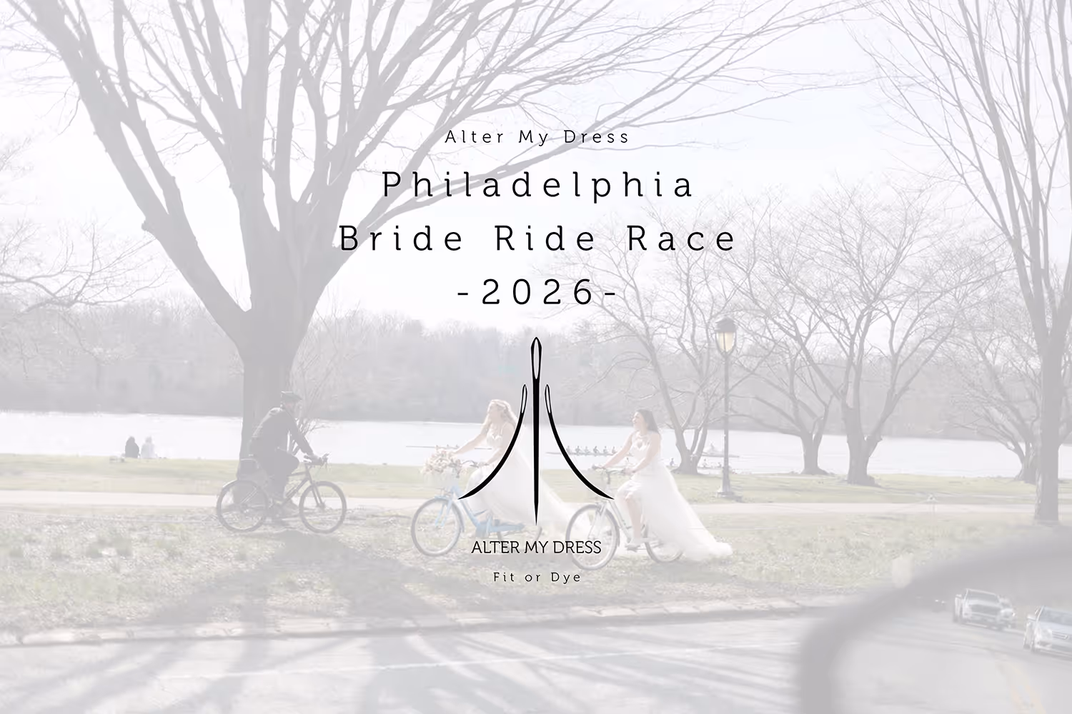 Two brides wearing wedding dresses riding bicycles beside a river in a park during the day, with a man on a bike nearby and leafless trees in the background.