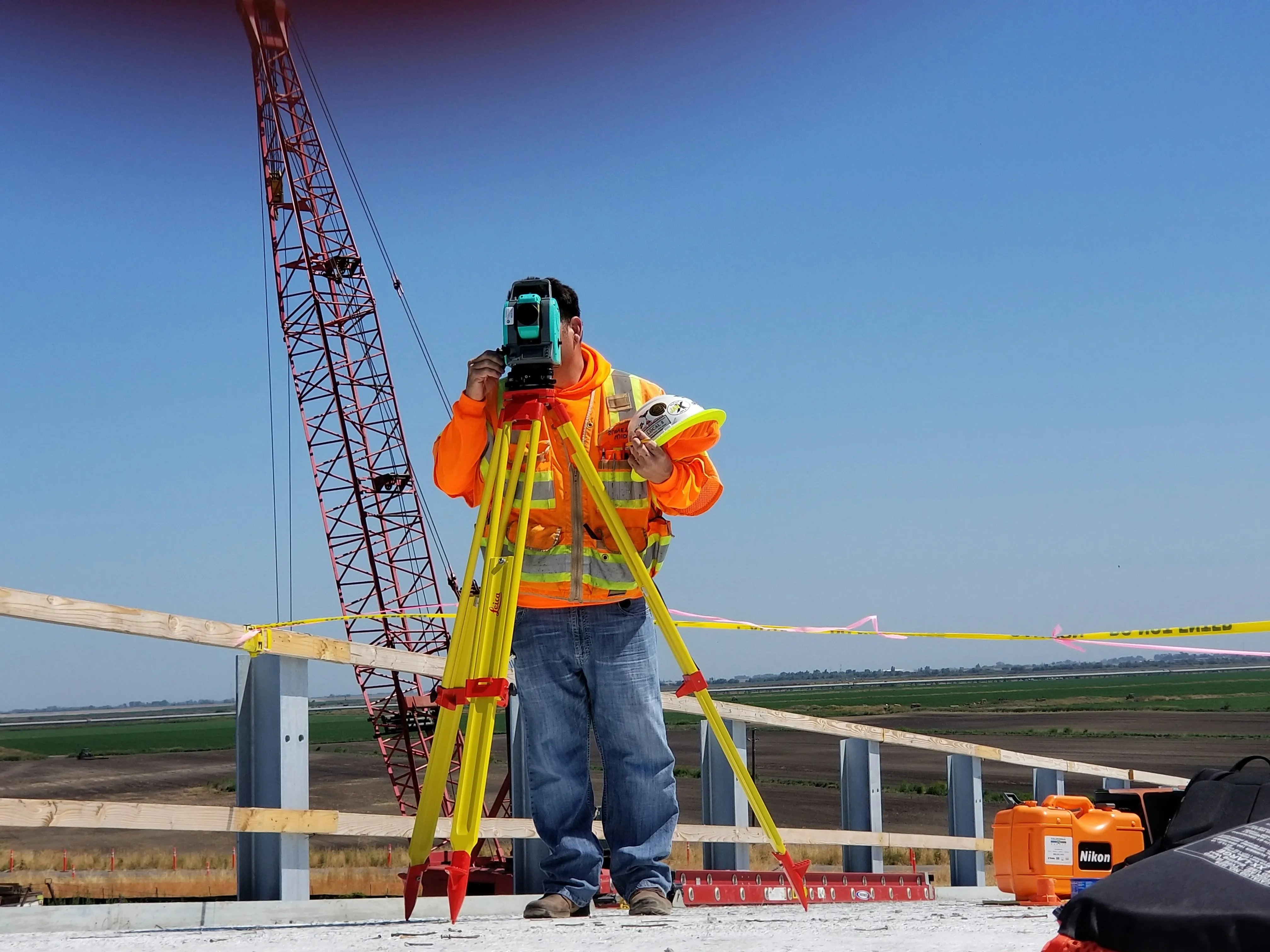 Surveyor using total station on construction site with crane