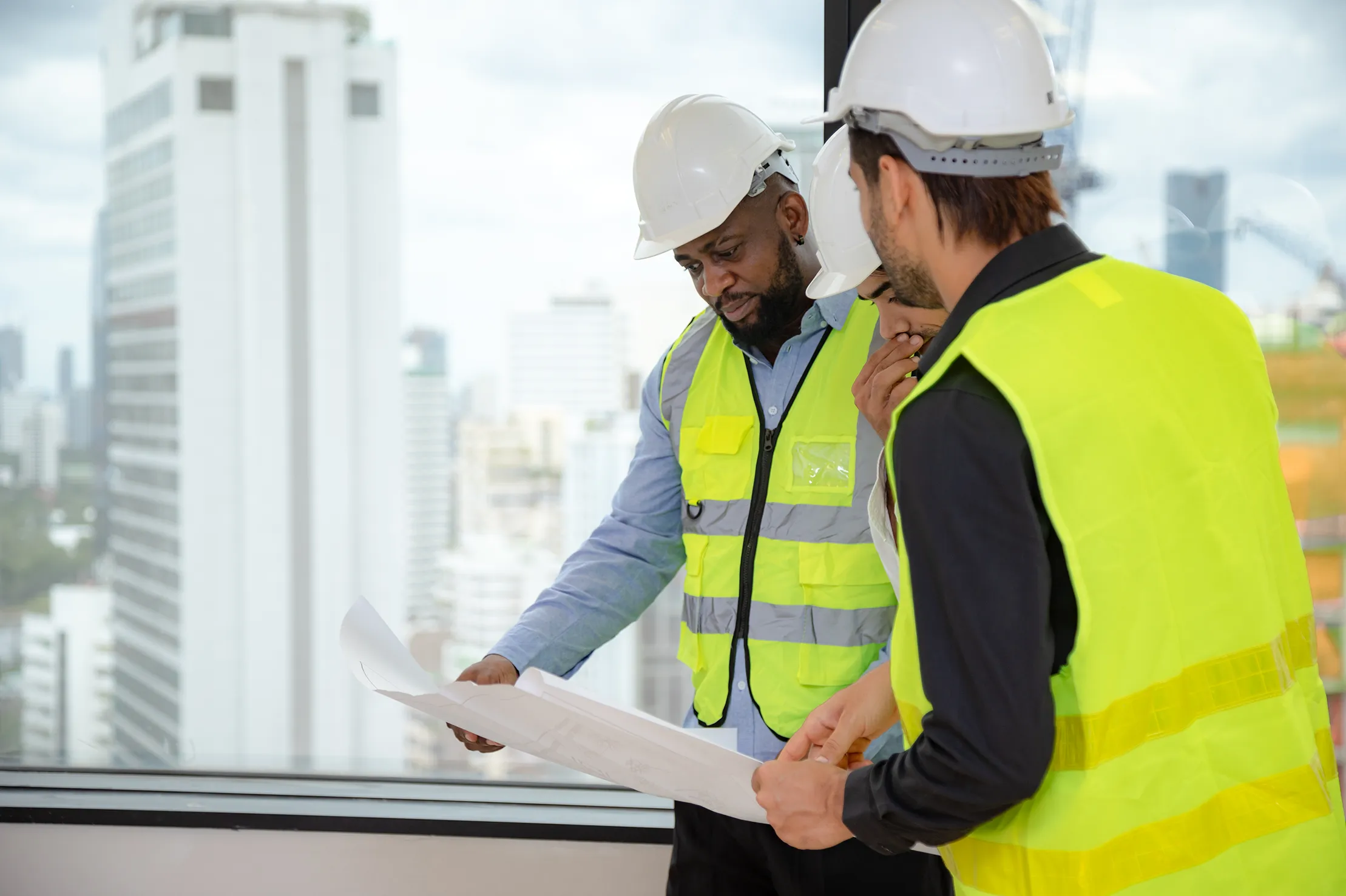 Construction workers in safety vests review blueprints near city window