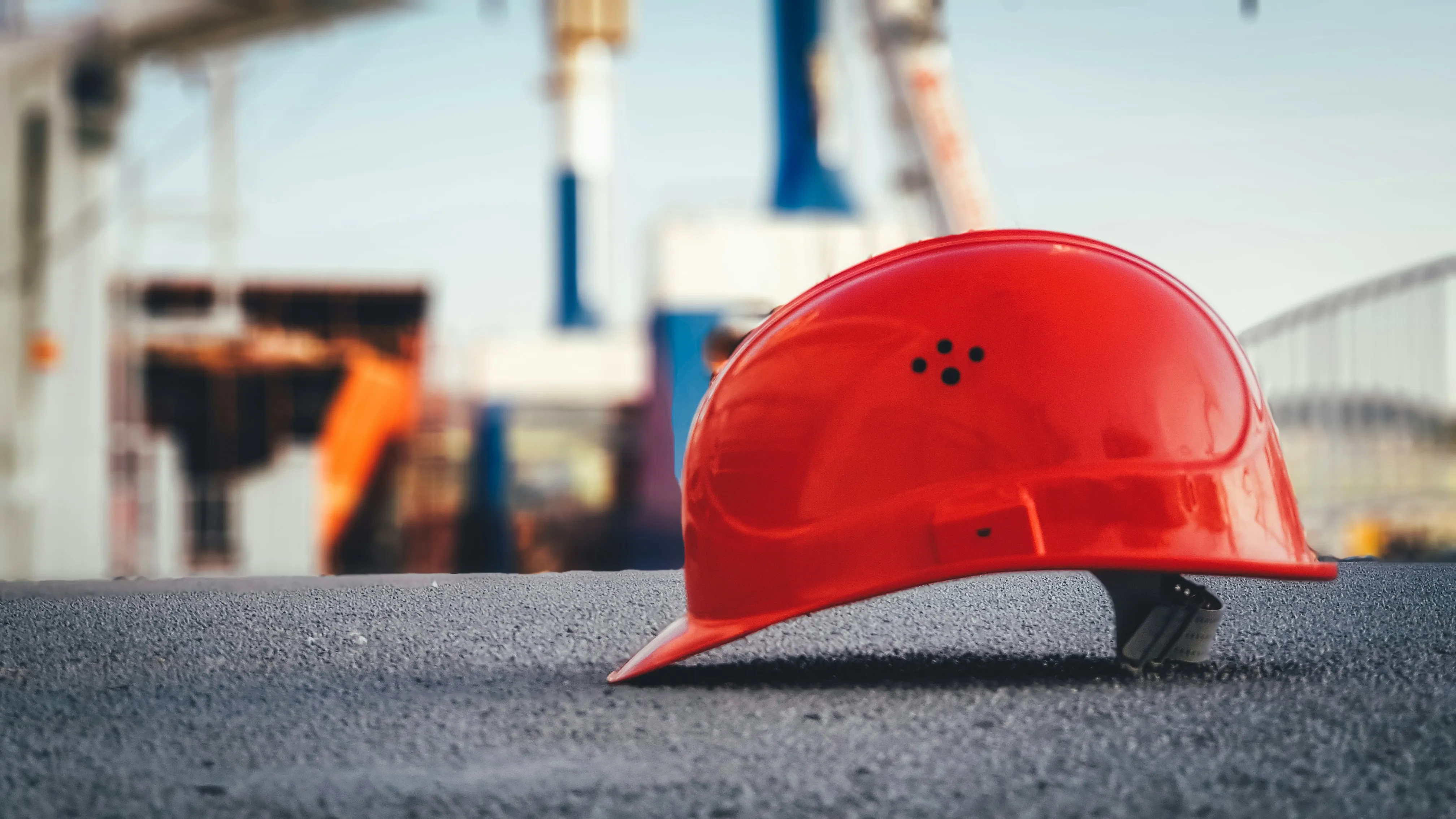 Bright red safety helmet on textured surface with construction site background