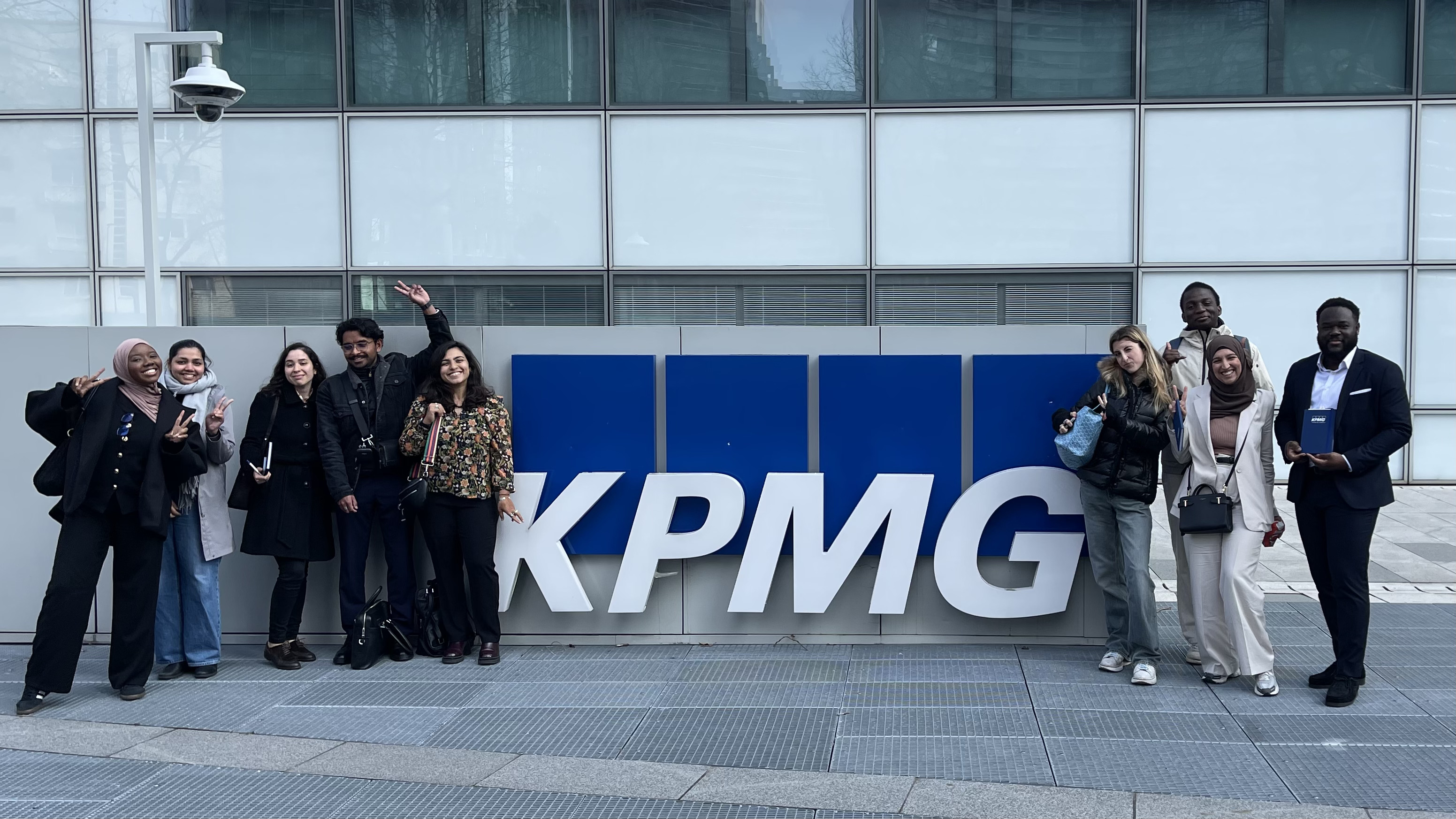 Groupe de jeunes posant devant le logo KPMG lors d'une visite d'entreprise, dans un cadre urbain moderne