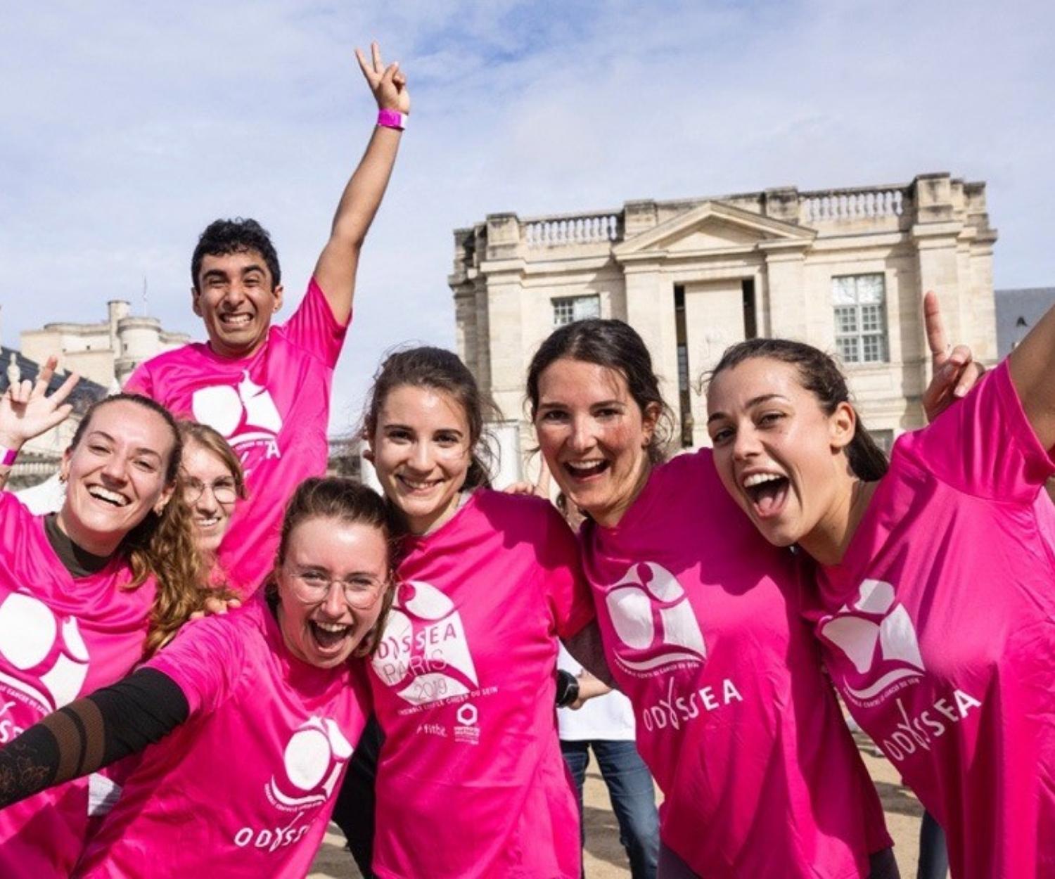 Group of smiling participants wearing pink T-shirts during an Odyssea solidarity race organized to support the fight against breast cancer.