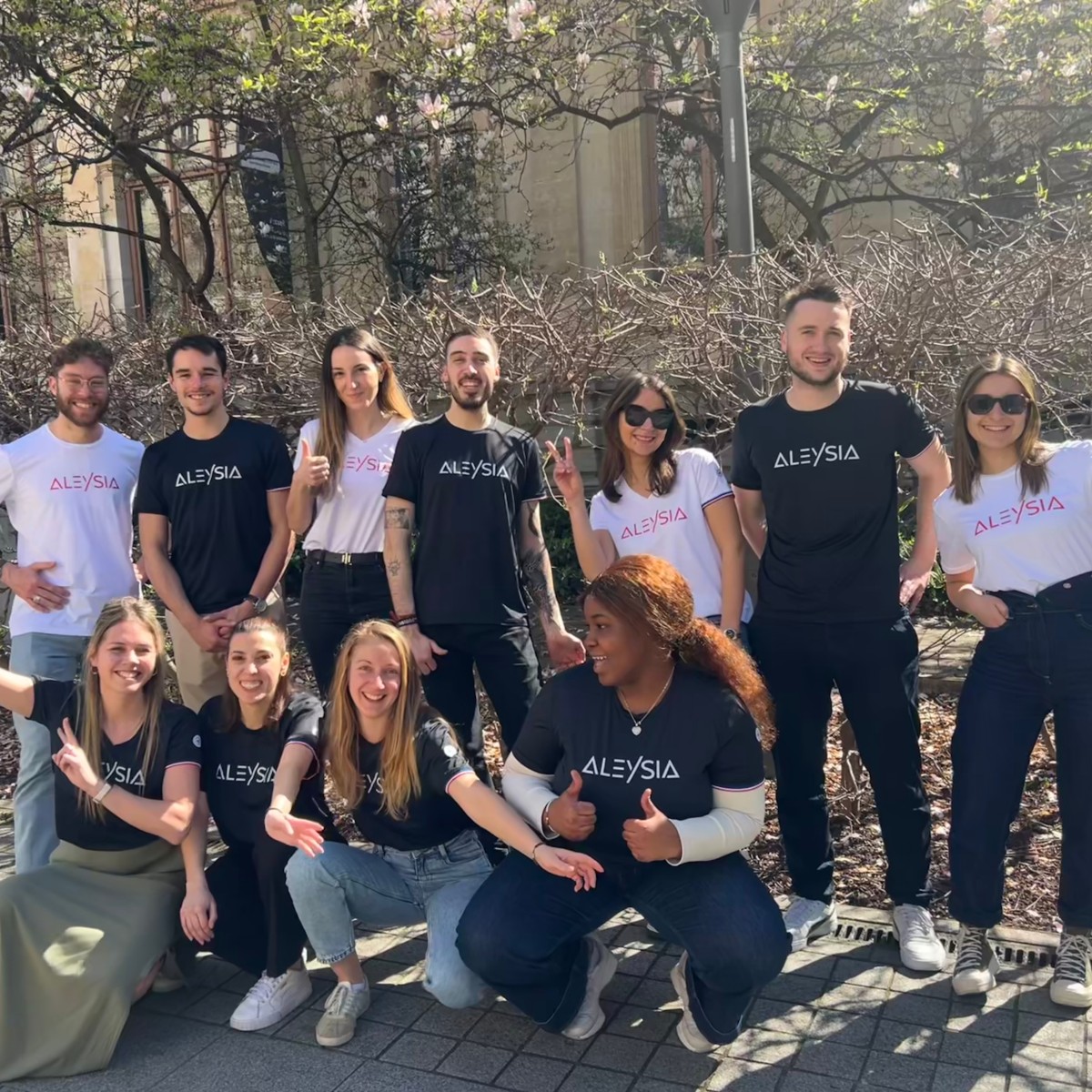 Équipe ALEYSIA posant en extérieur lors d’un moment convivial, portant des t-shirts aux couleurs de l’entreprise, ambiance ensoleillée et esprit d’équipe.