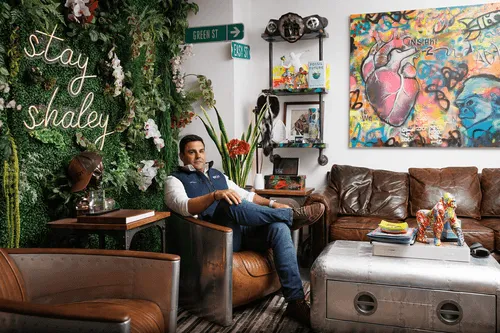 An image of a man sitting in front of a neon sign on a floral background.