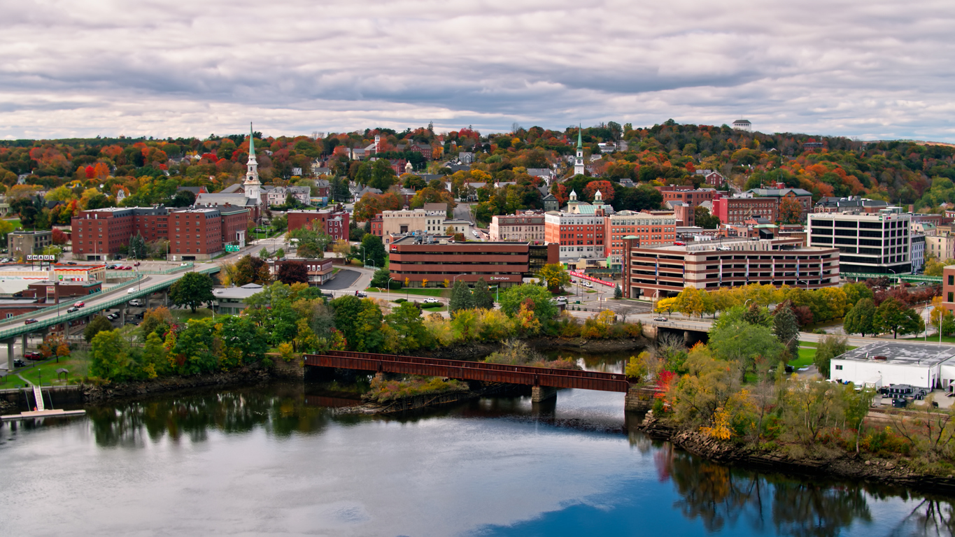 Aerial view of Bangor, Maine, the birthplace of Gorban Media, with a river, colorful trees, and buildings under cloudy skies.