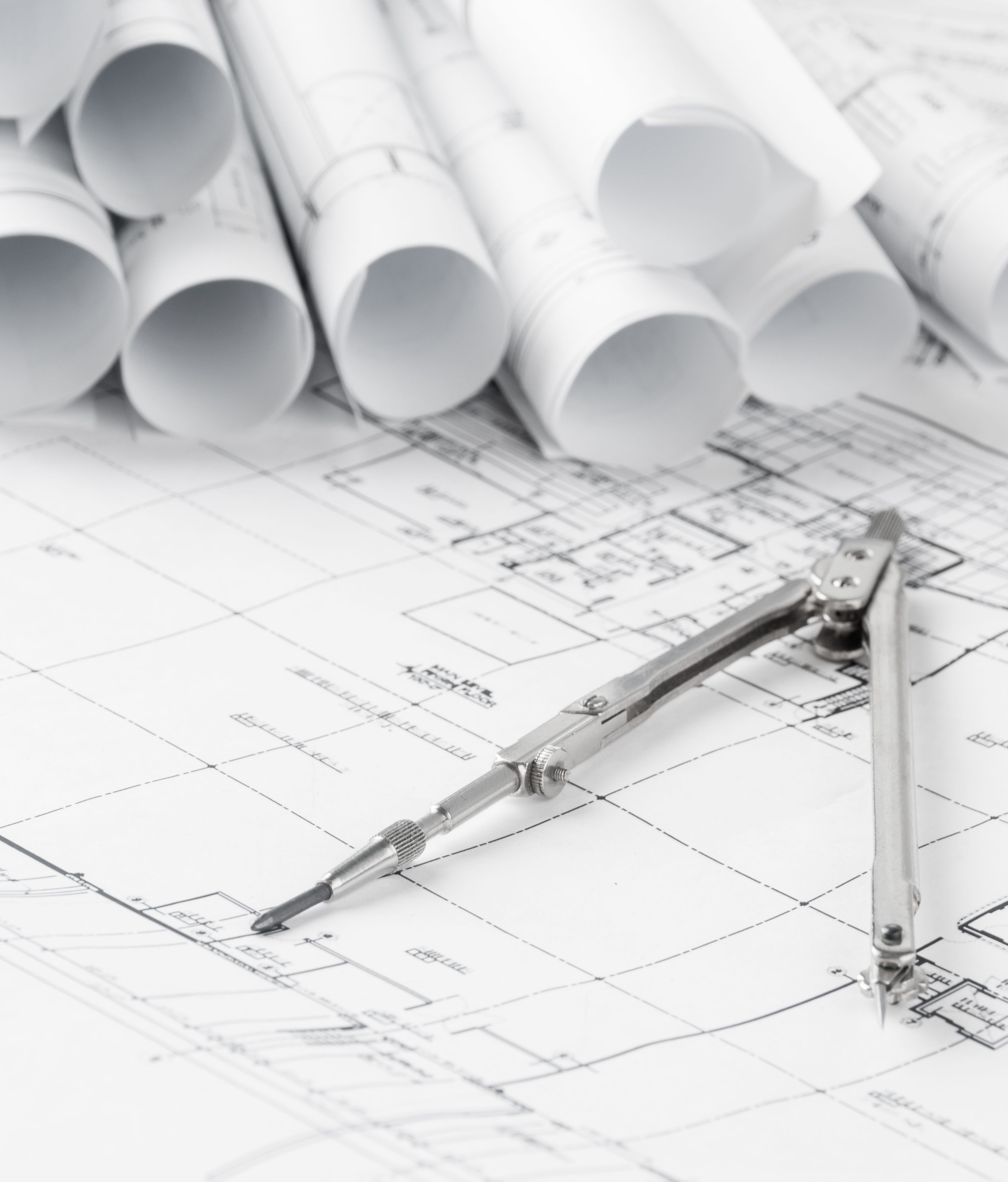 * A compass tool on blueprints surrounded by rolled-up architectural plans.