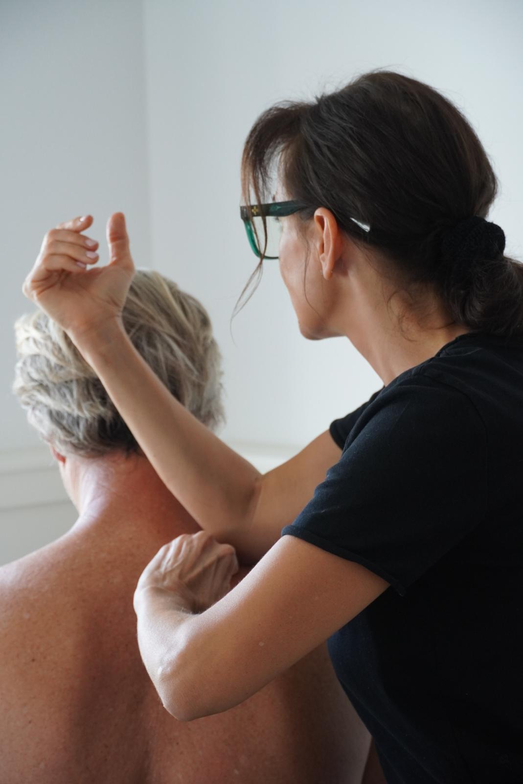 Fisioterapeuta realizando un tratamiento manual en la zona cervical y alta de la espalda de un paciente sentado.