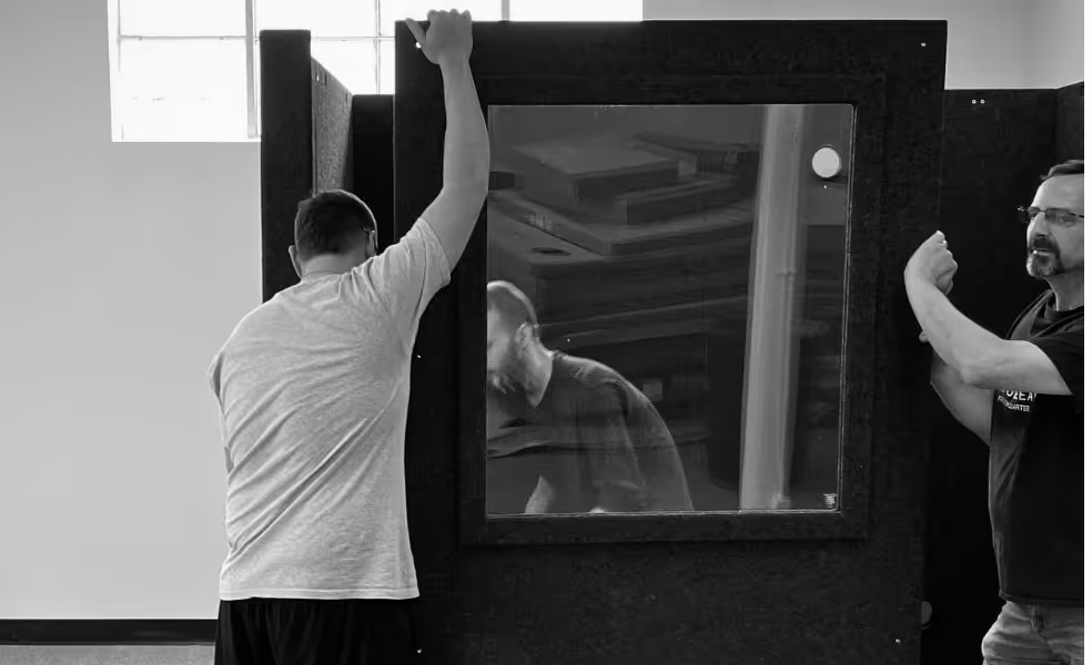 Two people assembling a WhisperRoom sound isolation booth panel during installation for a telehealth or private consultation space