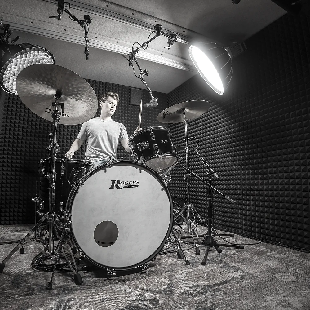 Jeff Randall playing a drum kit inside his WhisperRoom, the walls lined with acoustic foam and two studio lights overhead