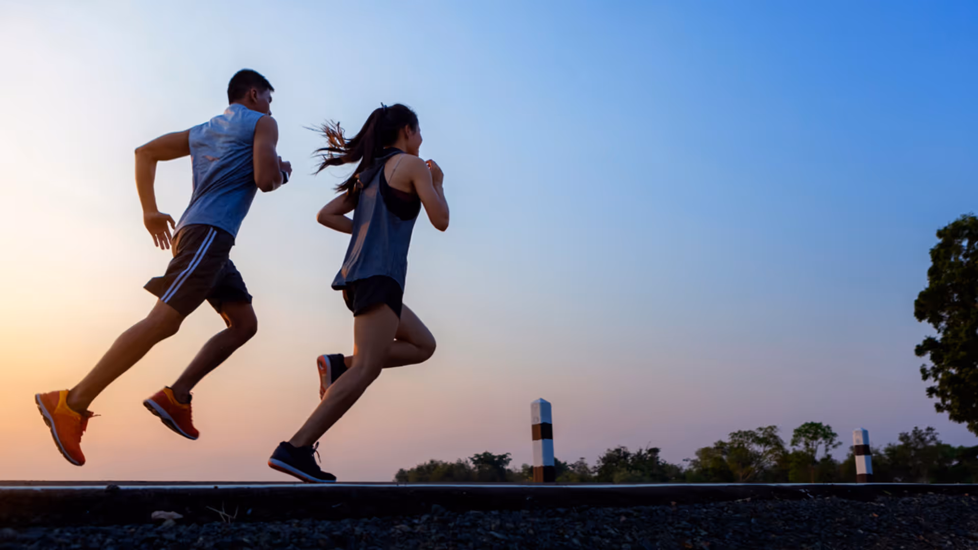 Man and woman running outdoors along a gravel path during sunset with a clear sky.