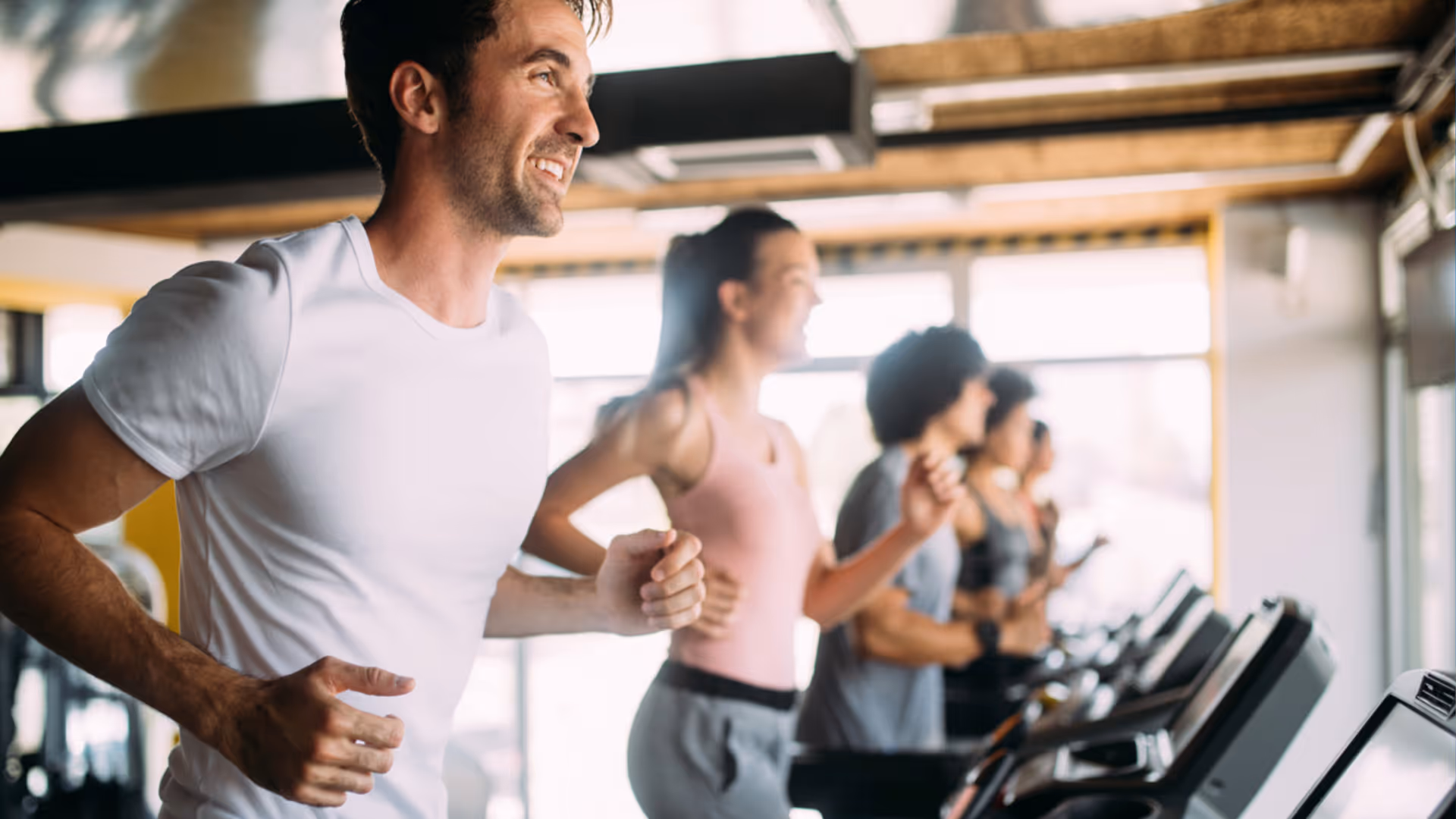 Group of diverse people running on treadmills in a bright gym.