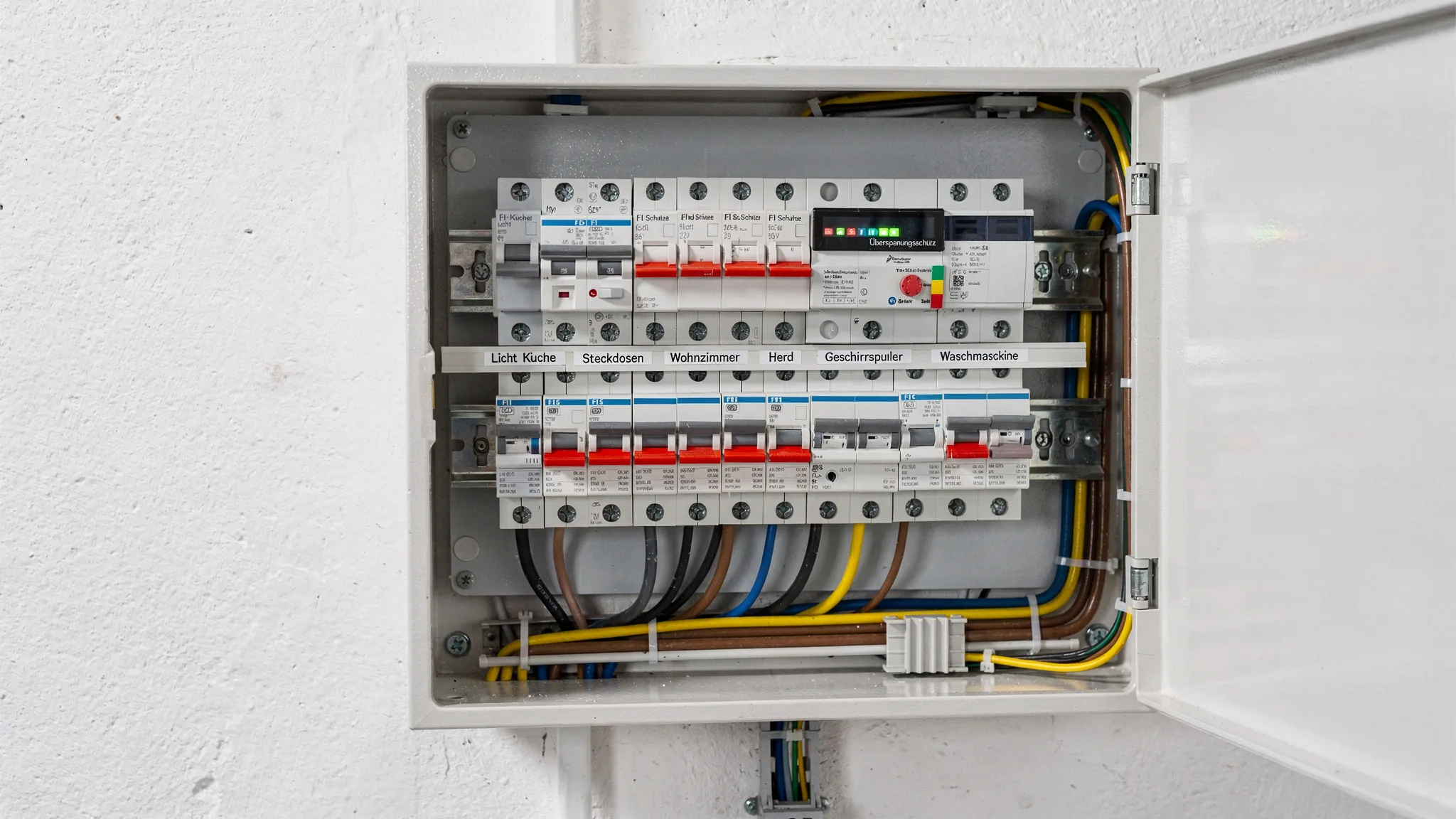 Ein moderner Zählerschrank mit sauber beschrifteten Sicherungsautomaten, RCD/FI-Schaltern, Überspannungsschutz und geordneten Leitungsabgängen in einem Technikraum.