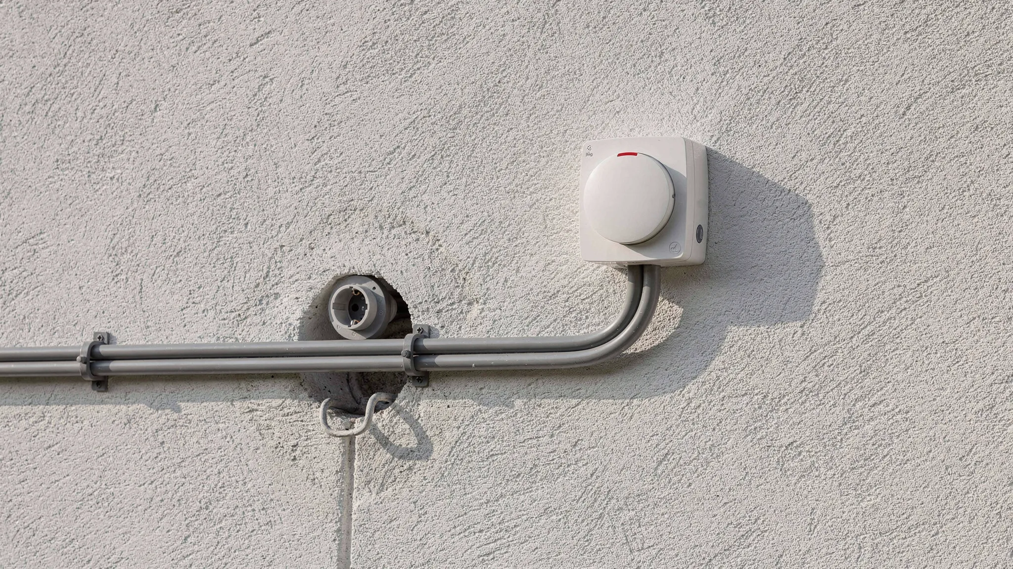 Außensteckdose und Außenleuchte an einer Hausfassade, Leitungsführung im geraden UV-beständigen Installationsrohr, saubere Wanddurchführung und Tropfschlaufe, Montage auf witterungsfester Fassade.