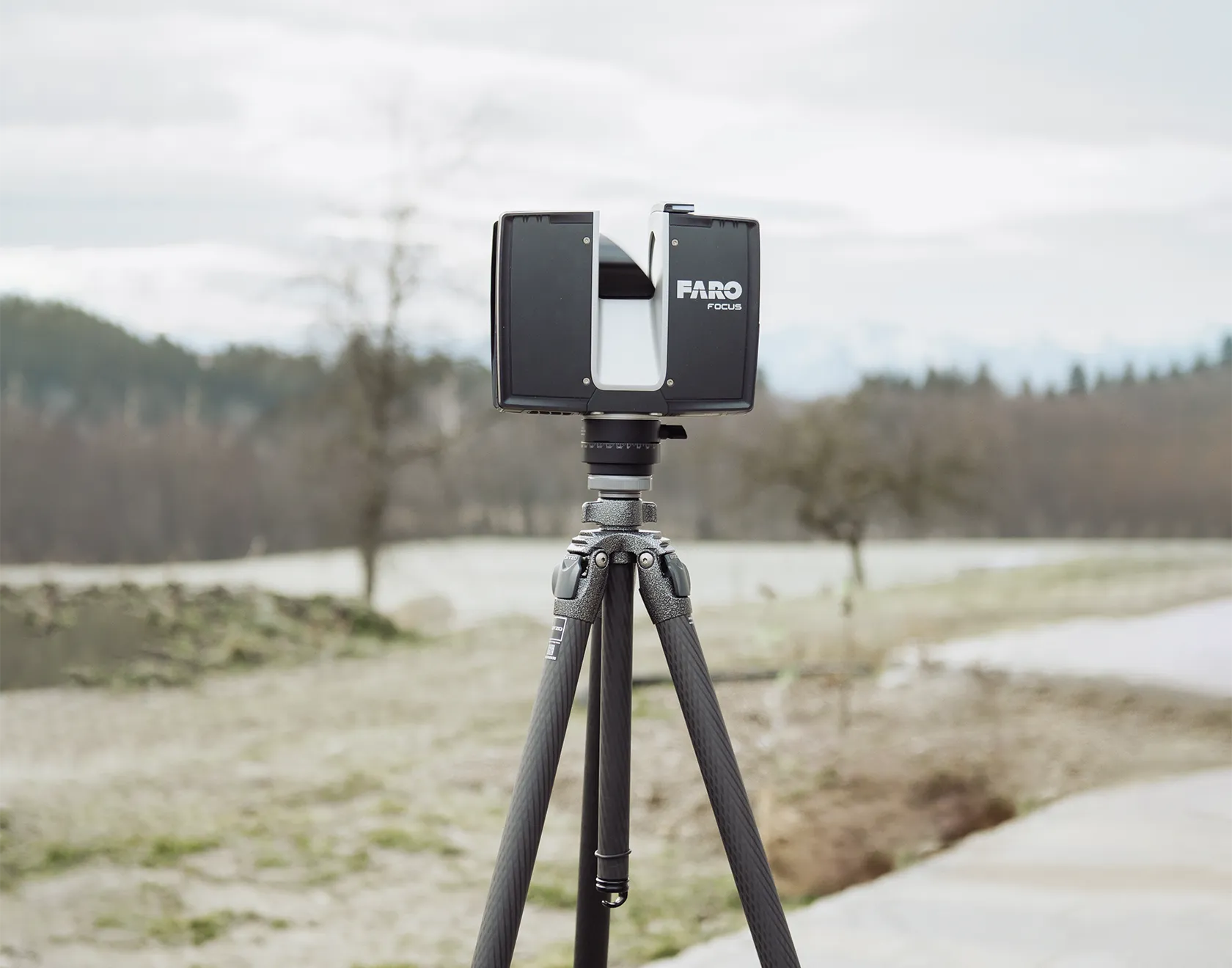 Ein FARO-3D-Laserscanner steht auf einem Stativ im Freien und erfasst die Umgebung für ein präzises Geländeaufmaß bei Neubauprojekten.