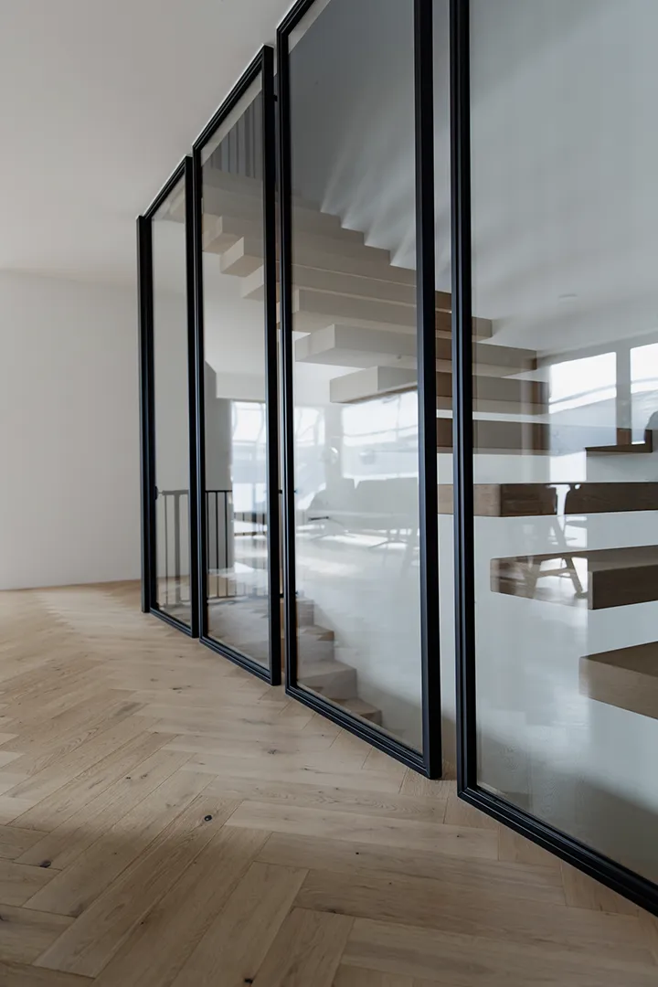 Innenansicht eines modernen Gebäudes mit Glaswänden und schwarzen Metallrahmen, die den Raum stilvoll strukturieren.
