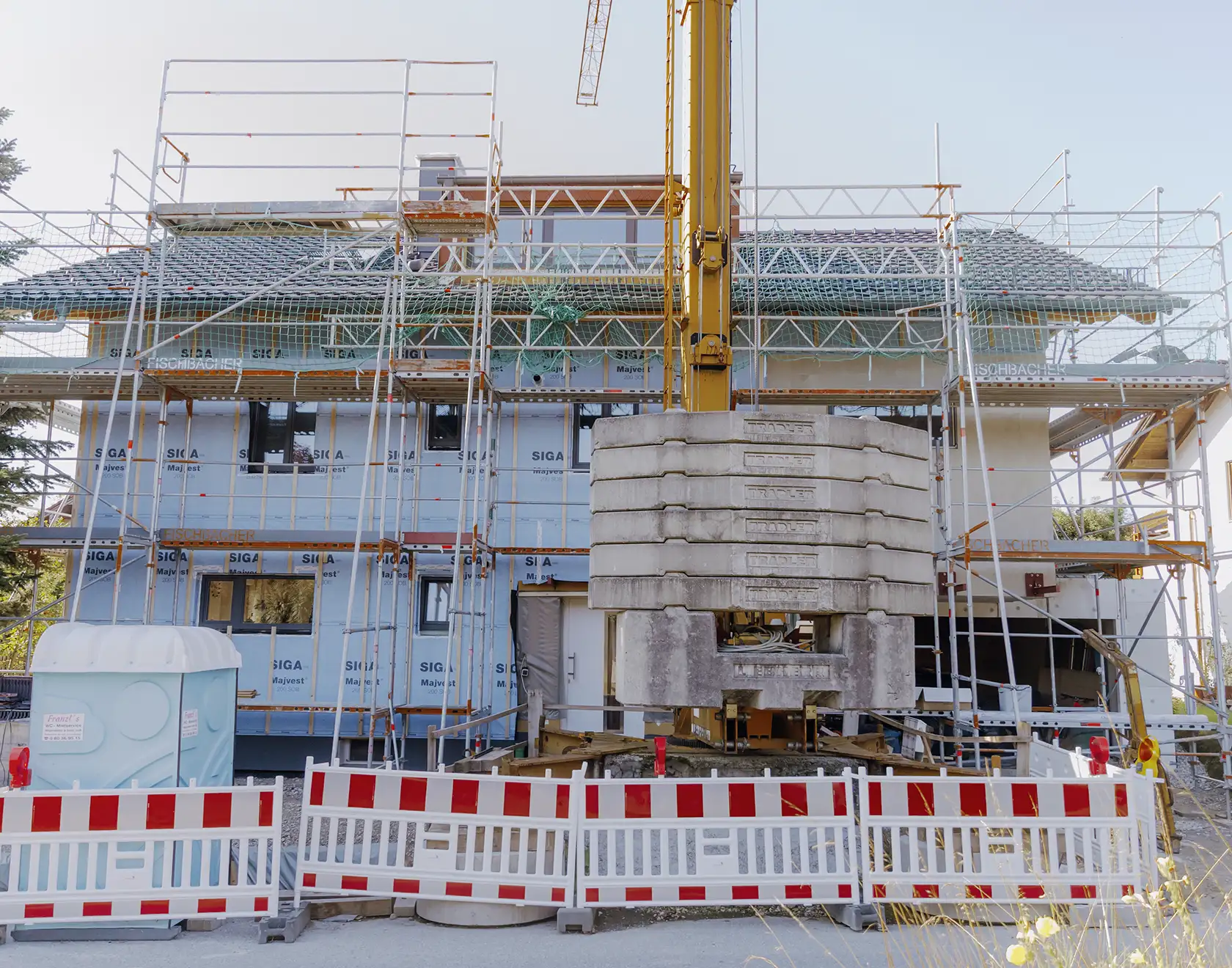 Ein Mehrfamilienhaus ist eingerüstet; eine Aufstockung mit neuen Holzbauelementen wird mithilfe eines Baukrans umgesetzt.