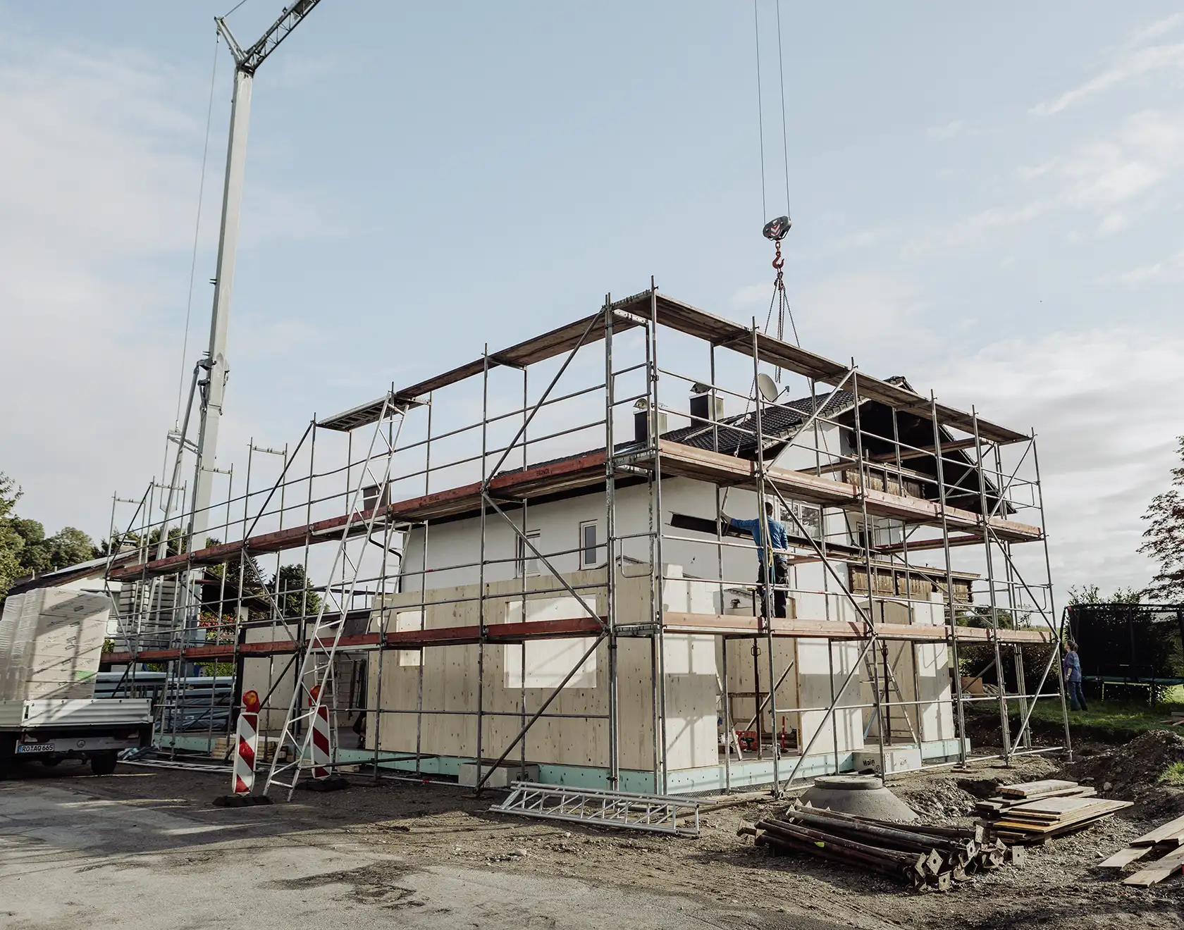 Ein Wohnhaus wird mit einem neuen Anbau erweitert; Baugerüst und Kran heben Holzelemente auf das bestehende Gebäude.