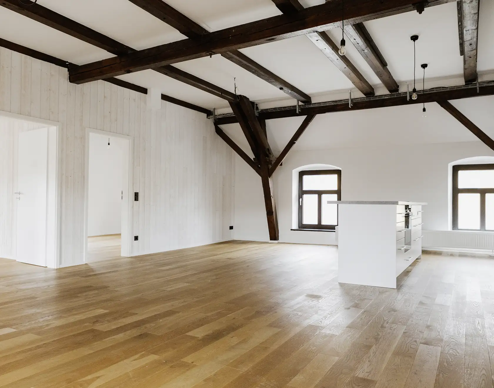 Ein heller, renovierter Dachraum mit sichtbaren Holzbalken und neuer Holzdecke; der Innenausbau ist nahezu abgeschlossen.