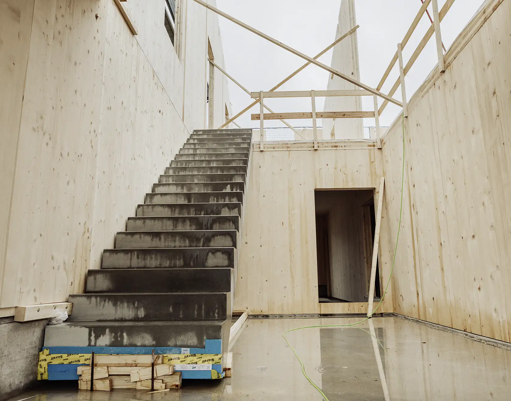 Eine Betontreppe und Holzwände in einem Rohbau zeigen den fortgeschrittenen Bauzustand eines Neubaus im Holzbauverfahren.