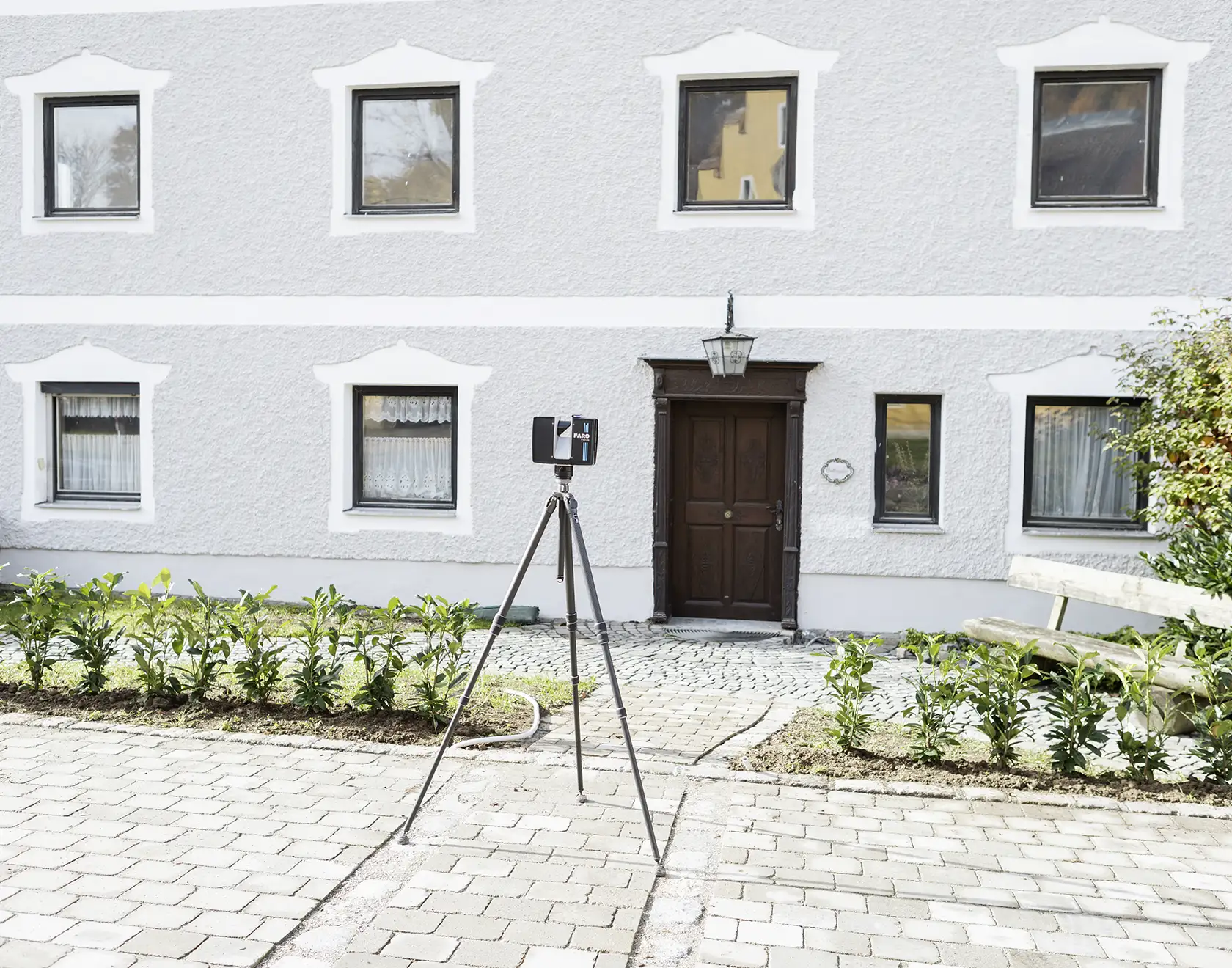 Ein 3D-Laserscanner steht vor einem Altbau mit grauer Putzfassade und Holz-Eingangstür, um die Gebäudefassade präzise zu vermessen.