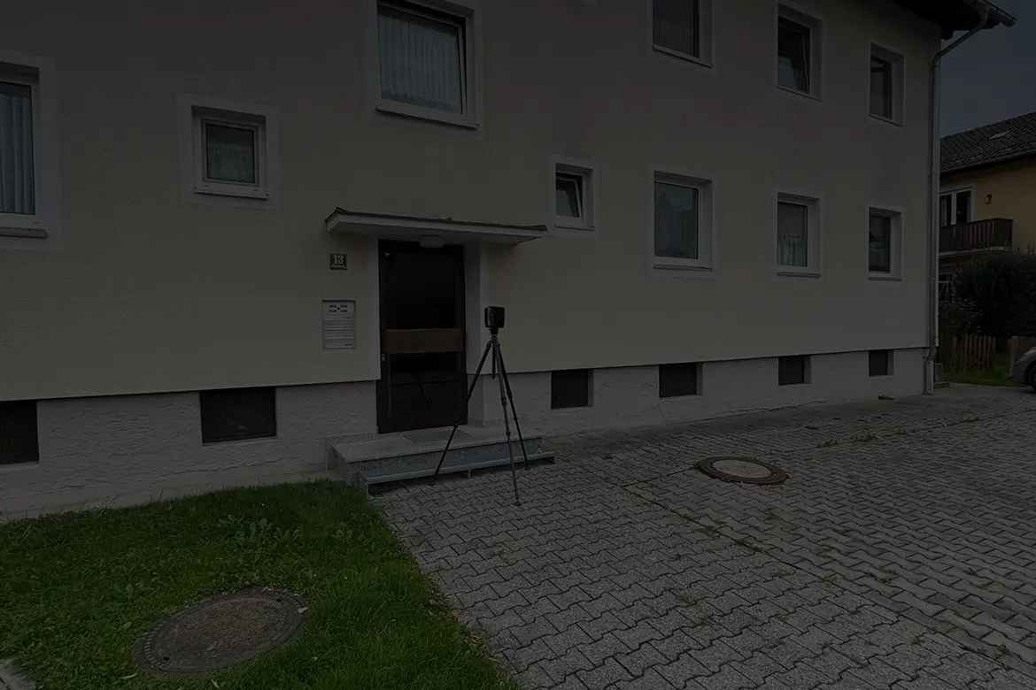 Ein 3D-Laserscanner steht vor einem Mehrfamilienhaus und erfasst die Fassade für die digitale Bauplanung.