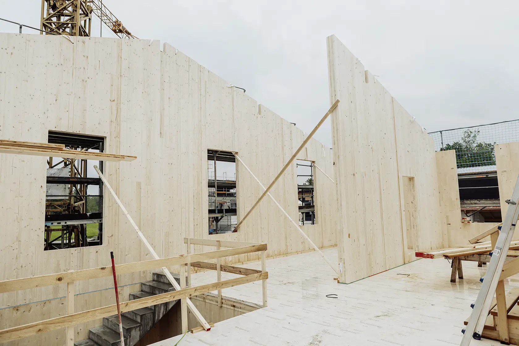 Baustelle mit teilweise errichteten, von Streben getragenen CLT-Wänden und Betontreppe.