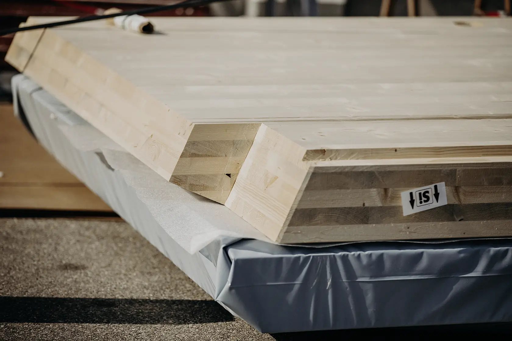 Ein Stapel hellfarbiger Holzbalken mit abgeschrägten Kanten liegt auf einer Schutzpolsterung.