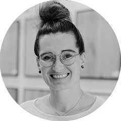 Anna-Lena, lächelnd mit dunklen Haaren und Brille vor verschwommenem Hintergrund. Portrait