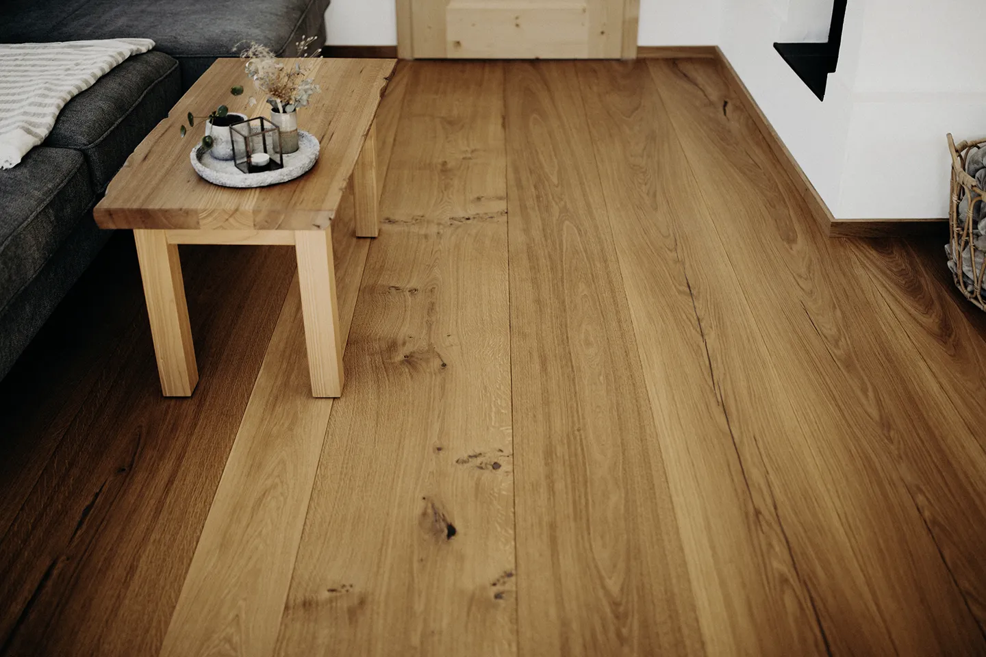Holzboden in einem Wohnzimmer mit einem Couchtisch aus Holz, einem grauen Sofa und Dekorationsgegenständen auf dem Tisch.