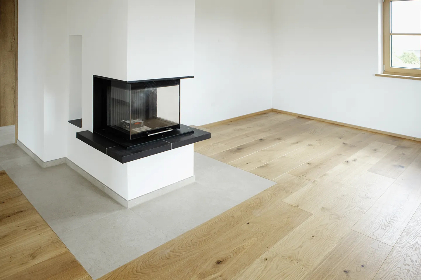 Eckkamin mit schwarzer Umrandung in einem Raum mit hellem Holzboden und weißen Wänden.