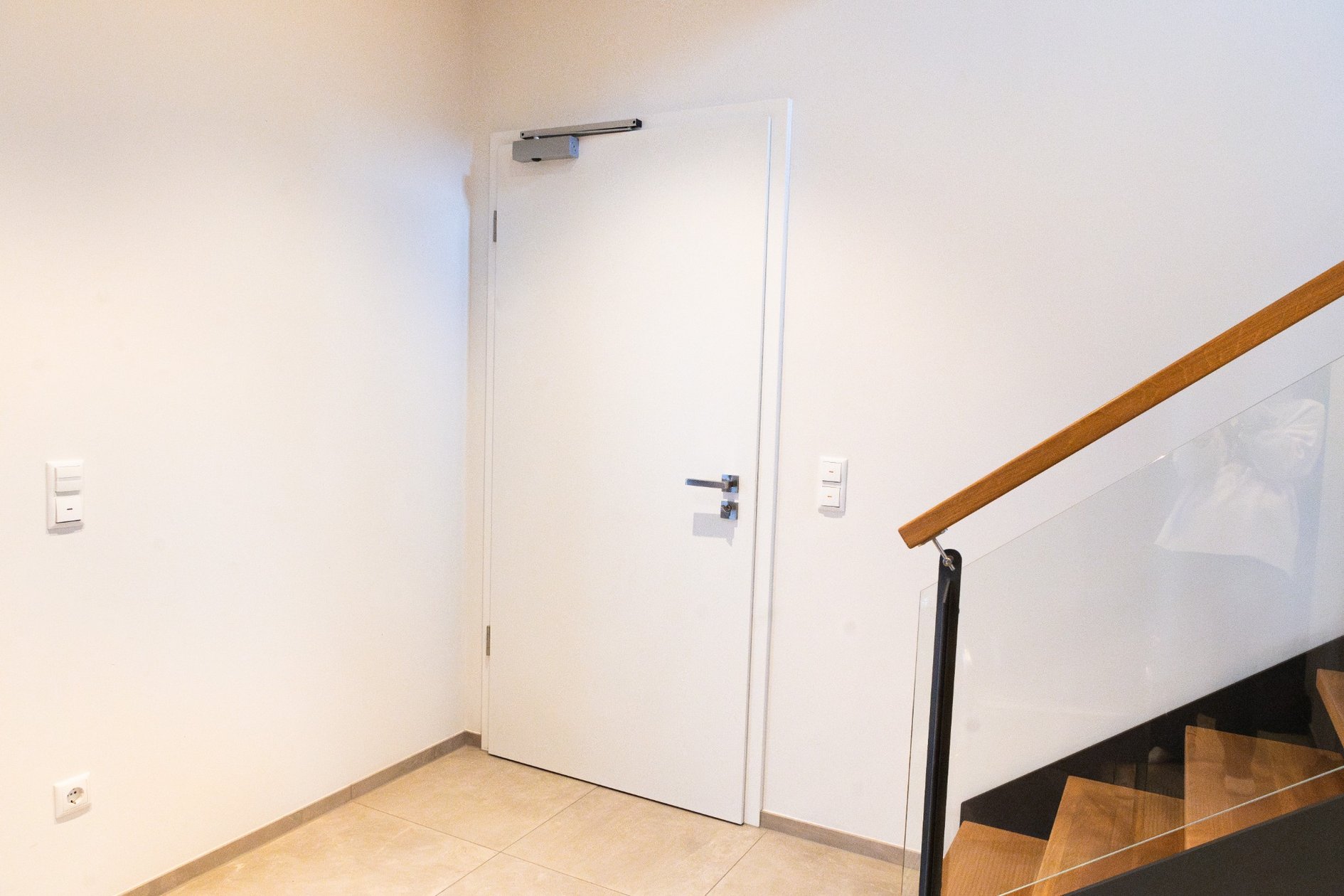 T30-Tür zur Garage mit Türschließer neben moderner Holztreppe