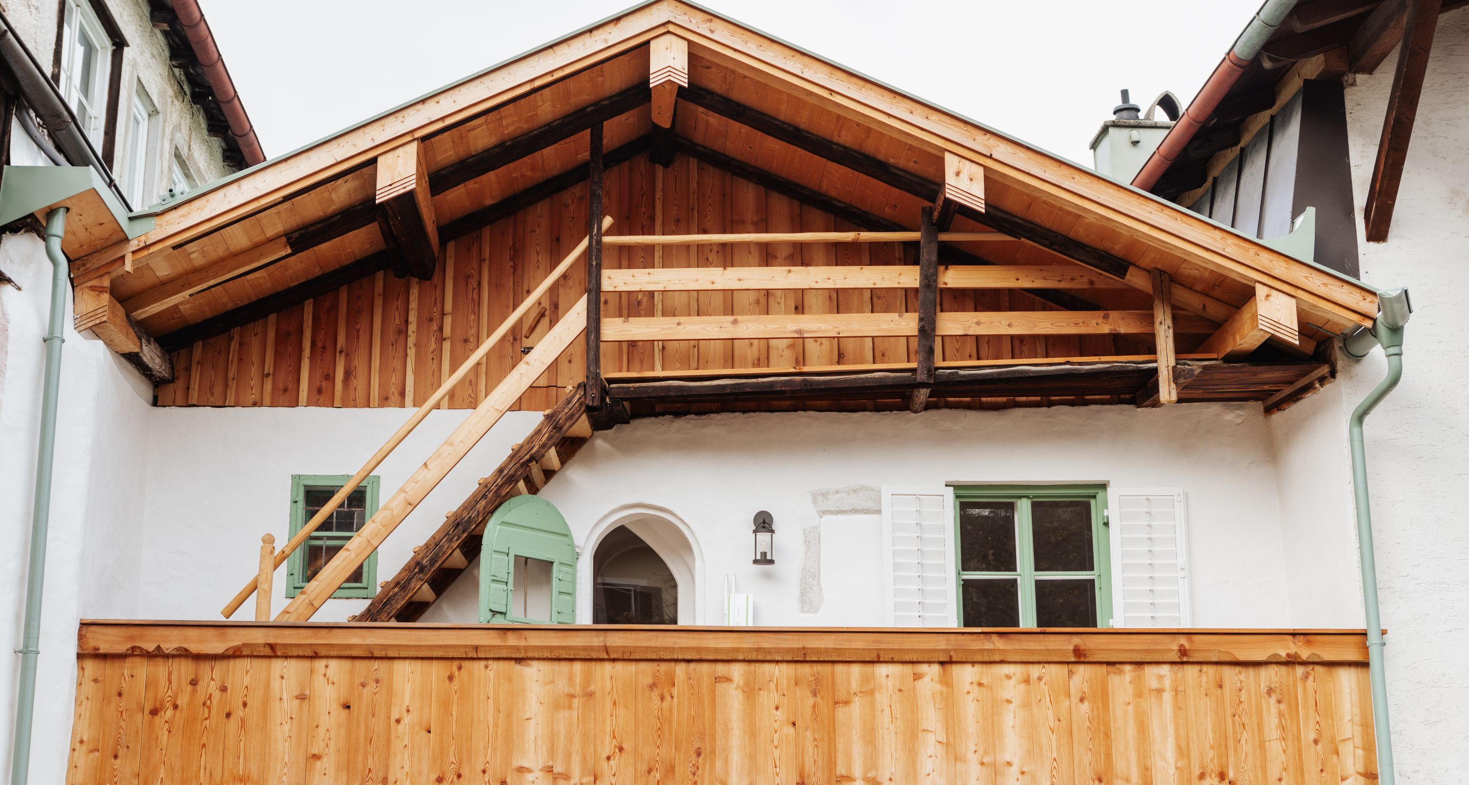 Detailaufnahme eines sanierten, denkmalgeschützten Holzhauses mit Balkon und grünem Fensterladen.