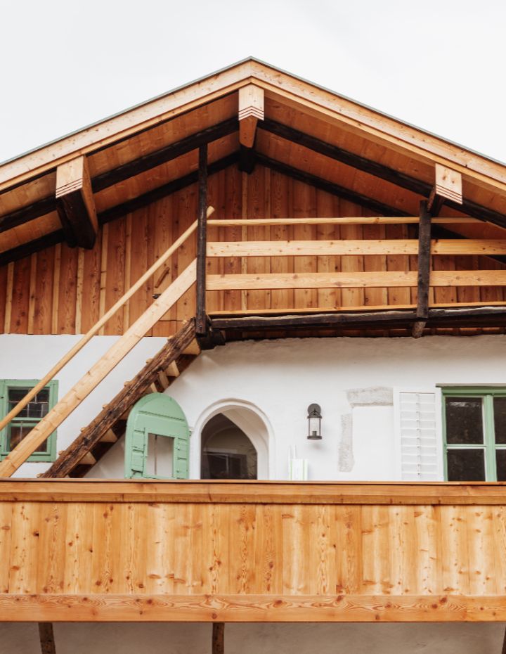 Detailaufnahme eines sanierten, denkmalgeschützten Holzhauses mit Balkon und grünem Fensterladen.