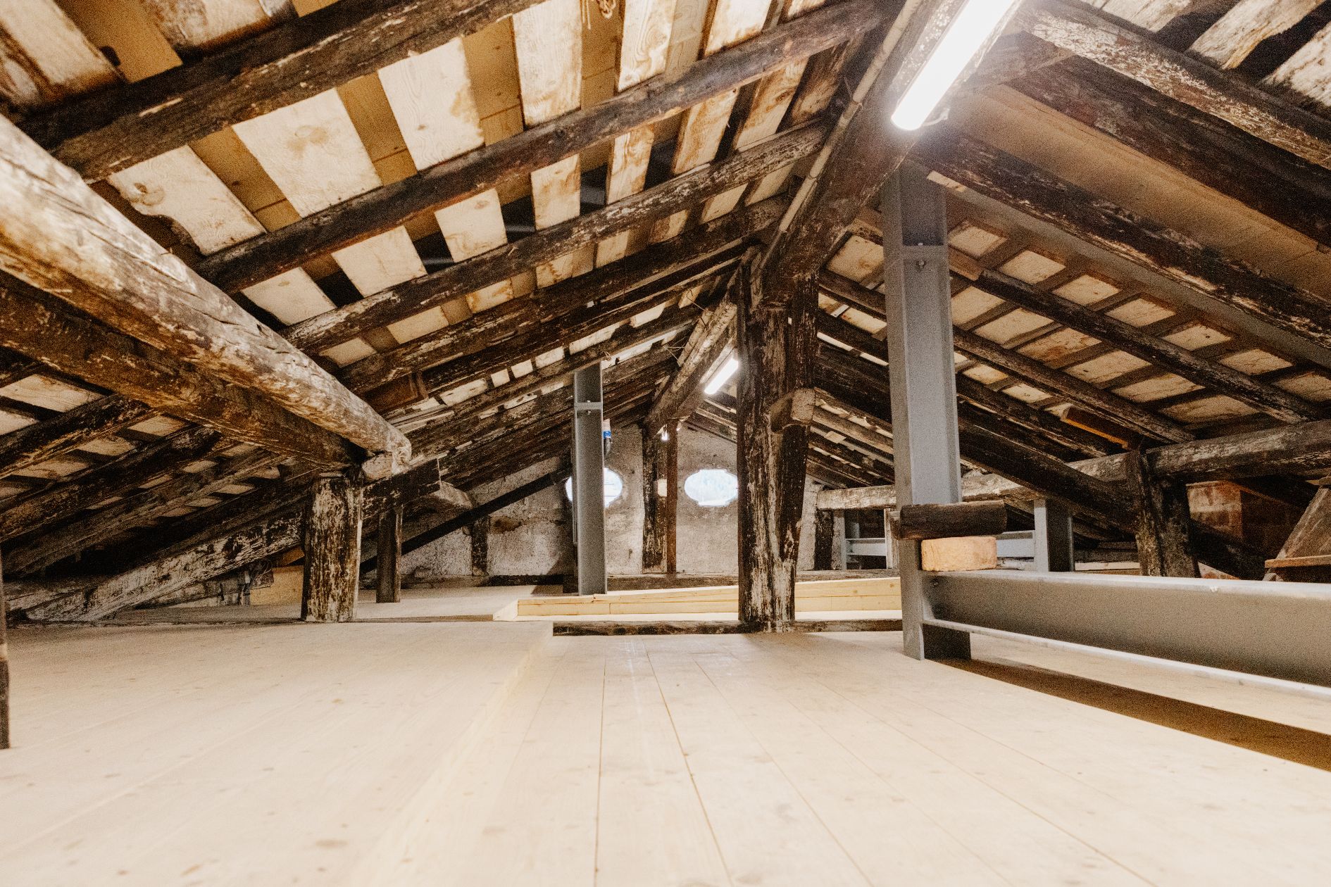 Blick in den historischen Dachstuhl des Brendlhauses in Bad Reichenhall mit sichtbaren alten Holzbalken und neu verlegtem Brettsperrholzboden.