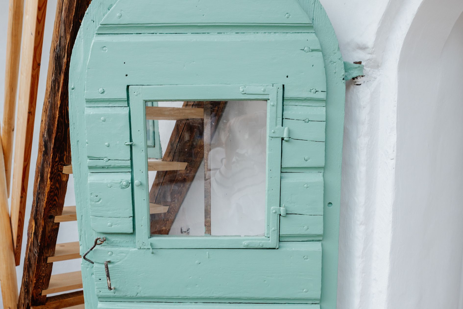 Detailaufnahme einer mintgrünen Holztür, dahinter sichtbar ist die neue Holztreppe im Innenhof.