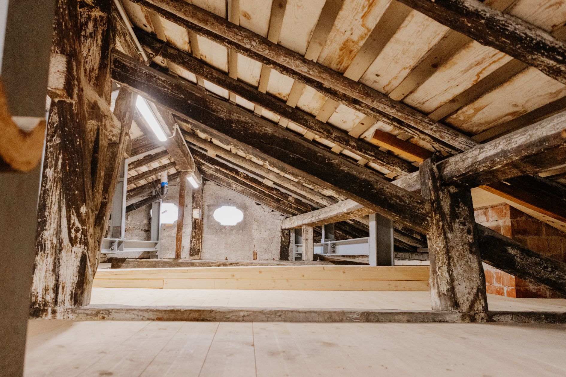 Blick in den historischen Dachstuhl des Brendlhauses. Alte, dunkle Balken treffen auf neue Brettsperrholzelemente.