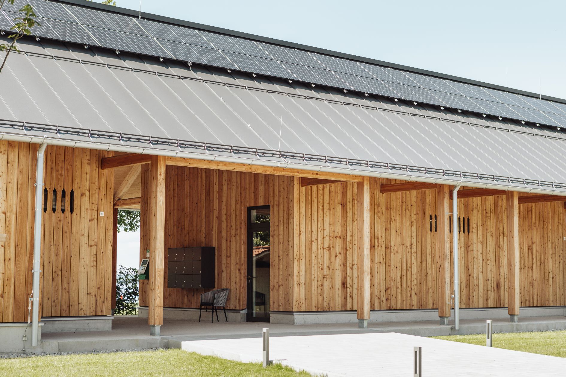 Außenansicht des Eingangsbereichs im Strandbad Felden mit Holzfassade, PV-Anlage auf dem Dach und überdachtem Vorbereich.
