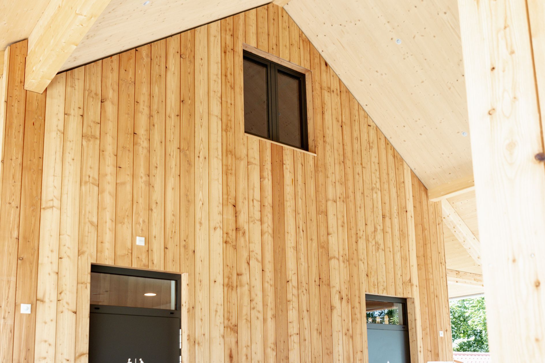 Holzfassade im Eingangsbereich des Strandbads Felden mit Fensteröffnung im Giebel und sichtbarer Brettsperrholzdecke.