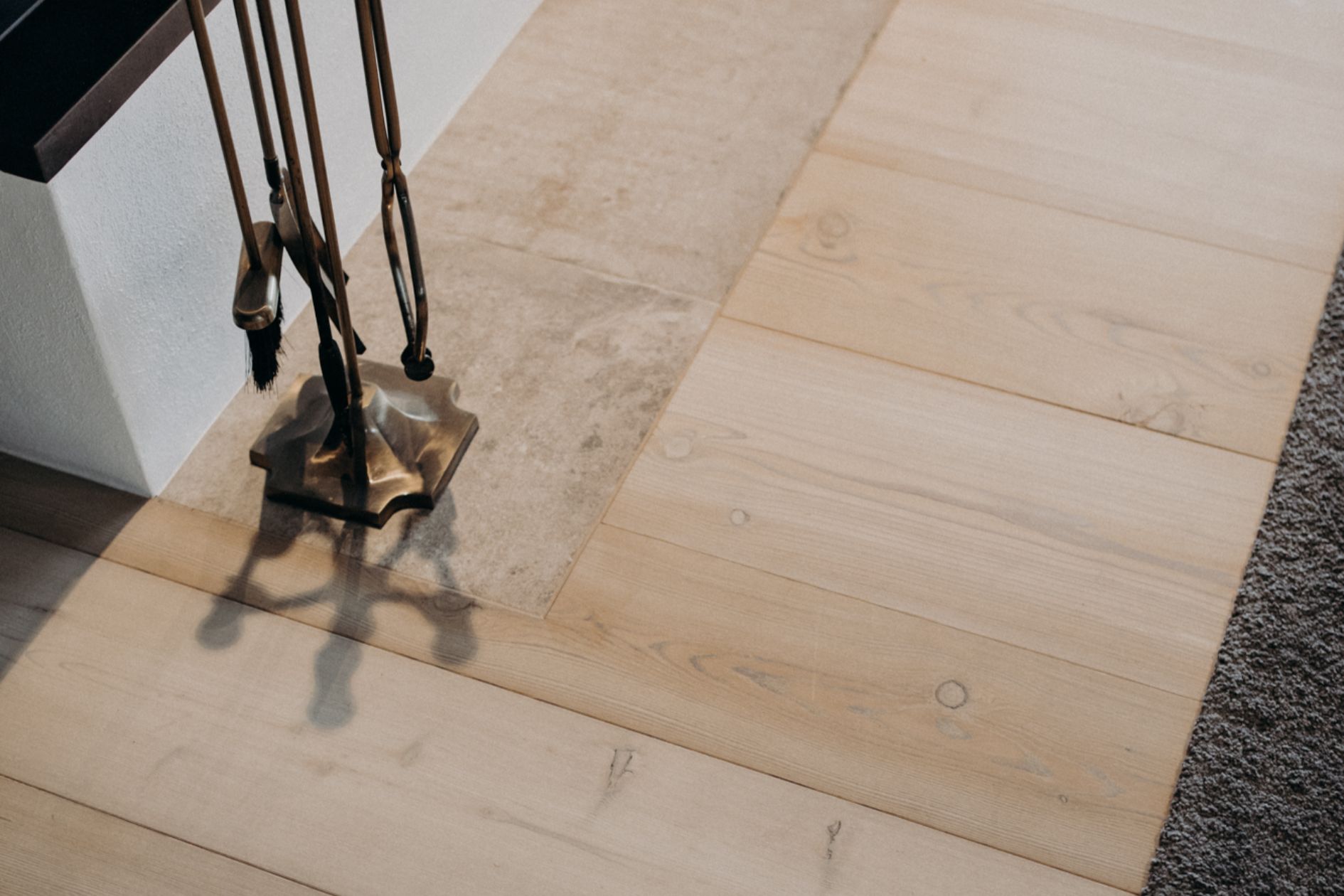 Detailansicht von weiß geölten Lärchendielen neben Natursteinplatten vor dem Kamin.