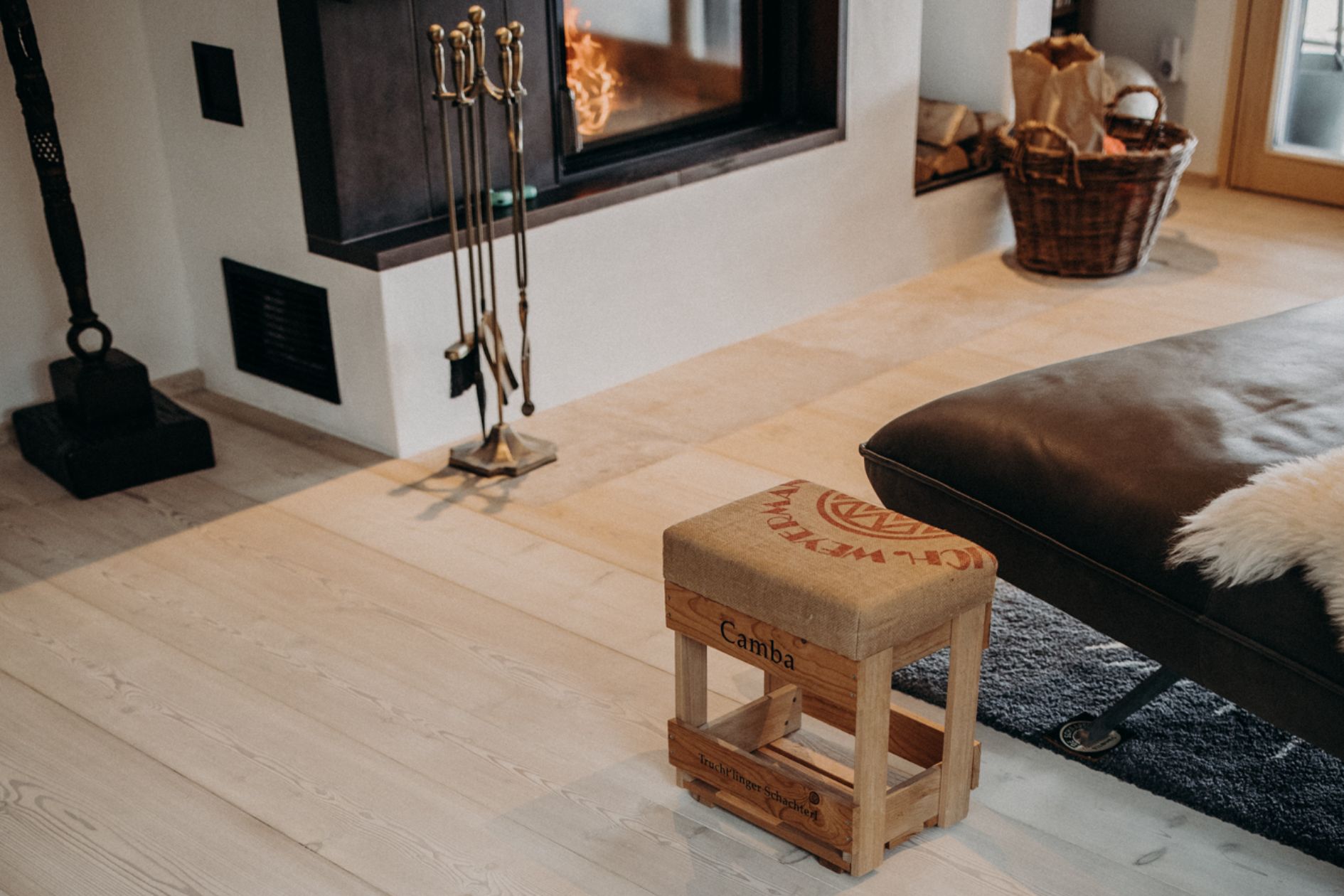Wohnbereich mit Kamin, raumlanger Lärchendiele in skandinavischem Look und kleiner Sitzbank aus Holz.