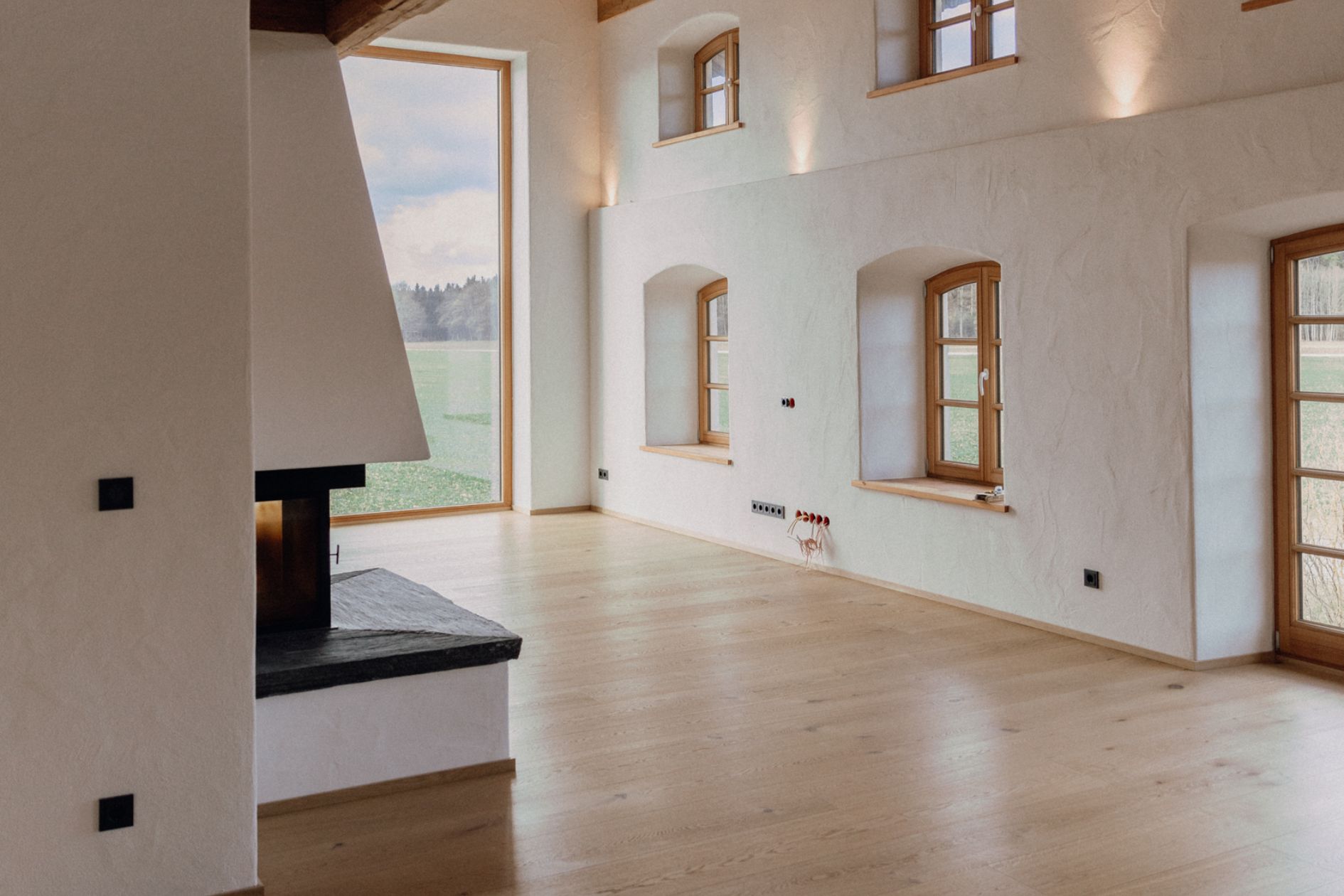 Heller Wohnraum mit geöltem Eichenboden, Kamin und großem Panoramafenster mit Blick auf die Wiese.