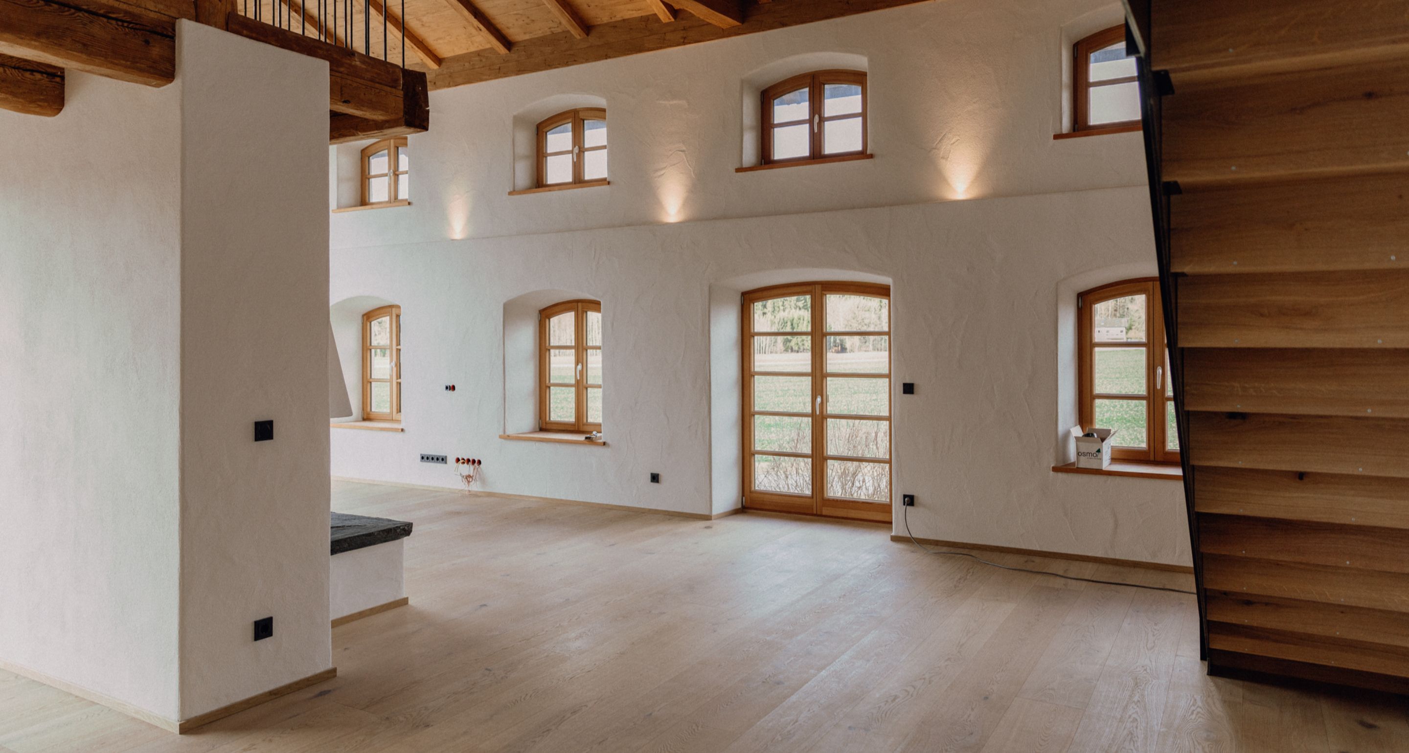 Heller Wohnraum mit geöltem Eichenboden, sichtbarer Balkendecke und rustikalen Holzfenstern.