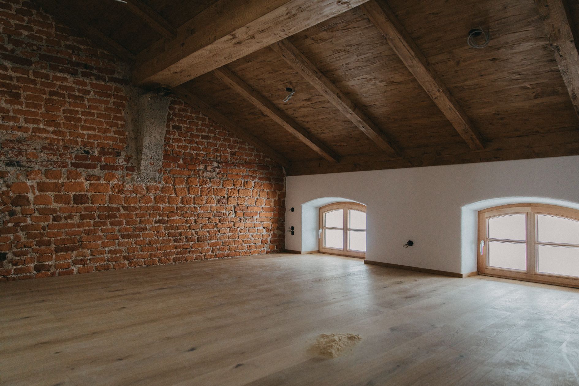 Renovierter Dachboden mit Ziegelwand, rustikaler Holzbalkendecke und geöltem Eichenboden.