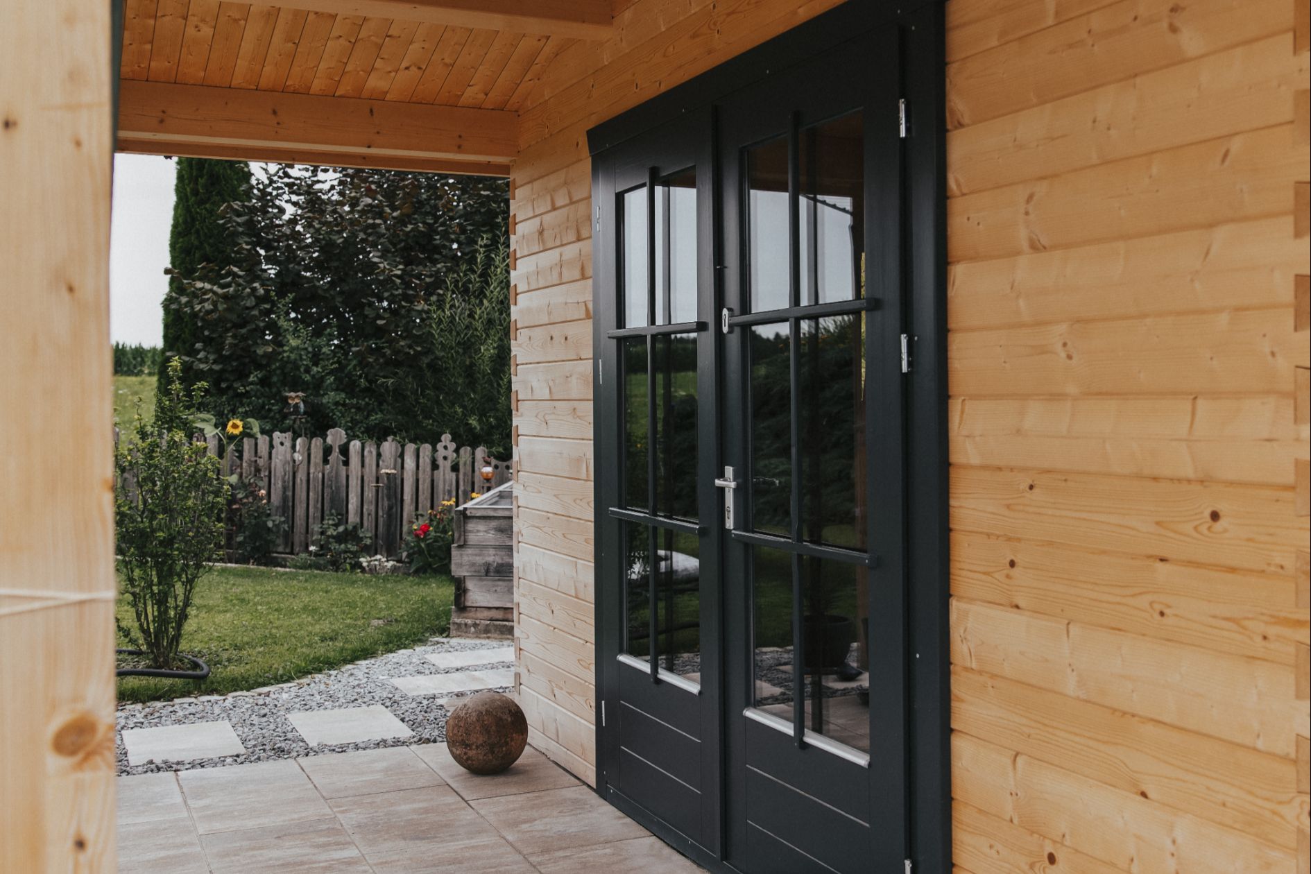 Detailansicht der dunklen Doppeltür eines Gartenhauses mit naturbelassener Holzfassade.