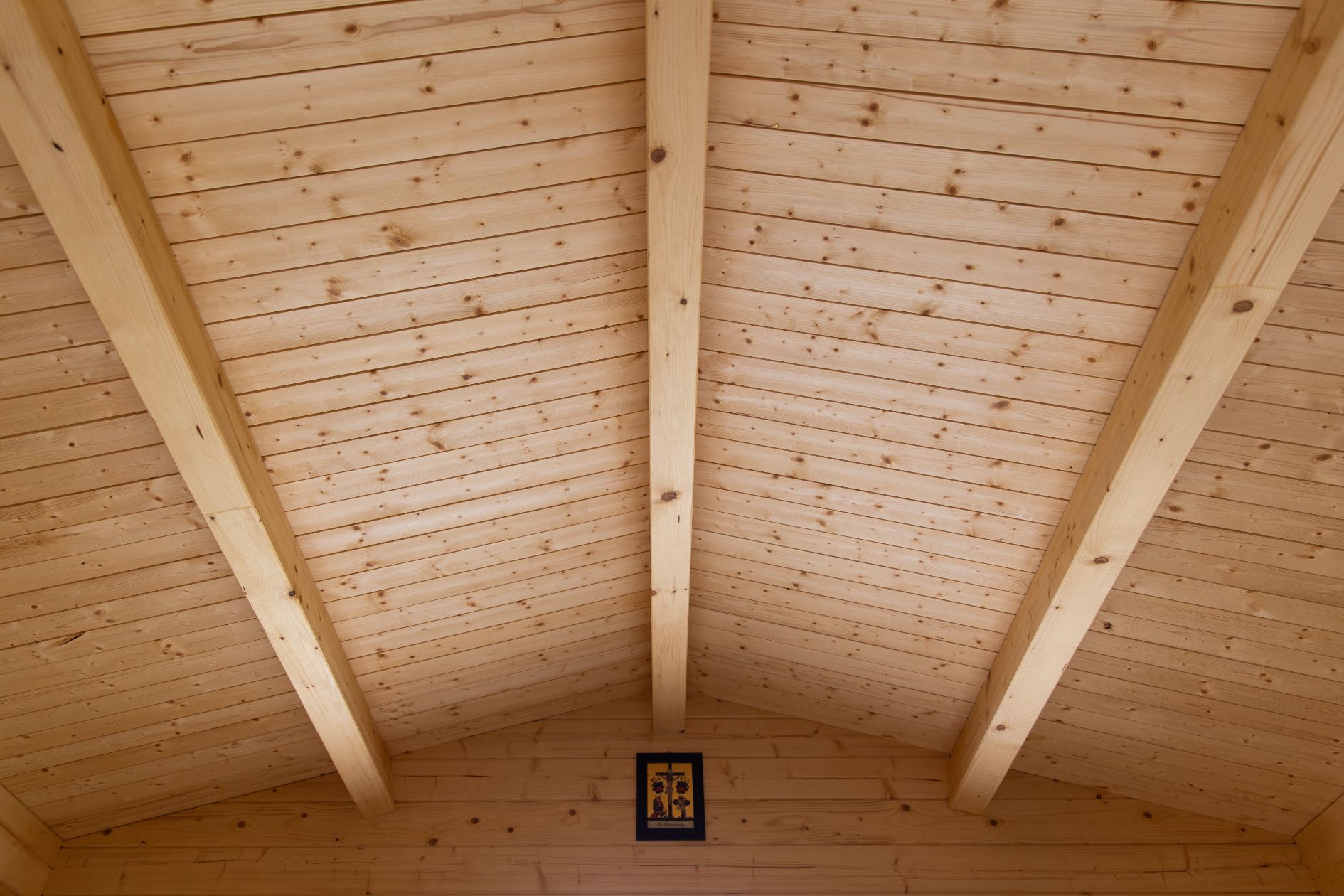 Detailaufnahme der sichtbaren Holzdecke mit Dachbalken im Innenraum eines Gartenhauses.