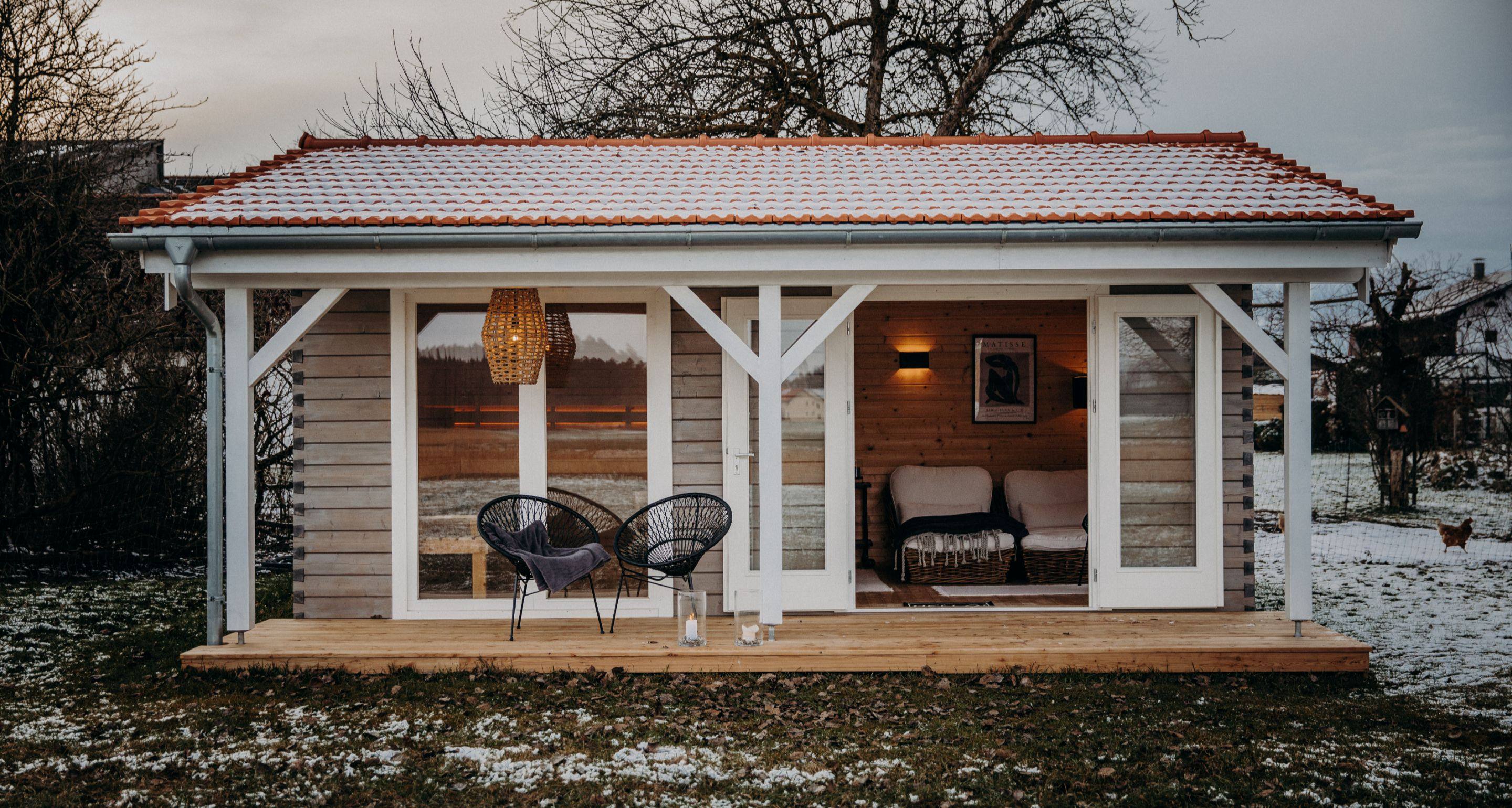 Modernes Saunahaus aus Holz mit überdachter Terrasse im winterlichen Garten.