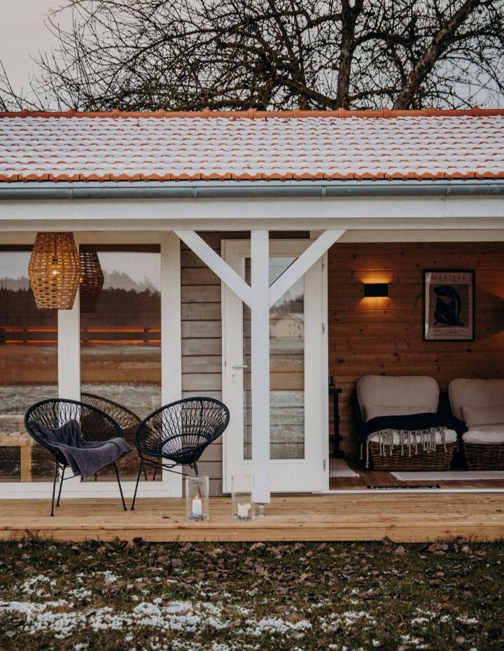 Modernes Saunahaus aus Holz mit überdachter Terrasse im winterlichen Garten.