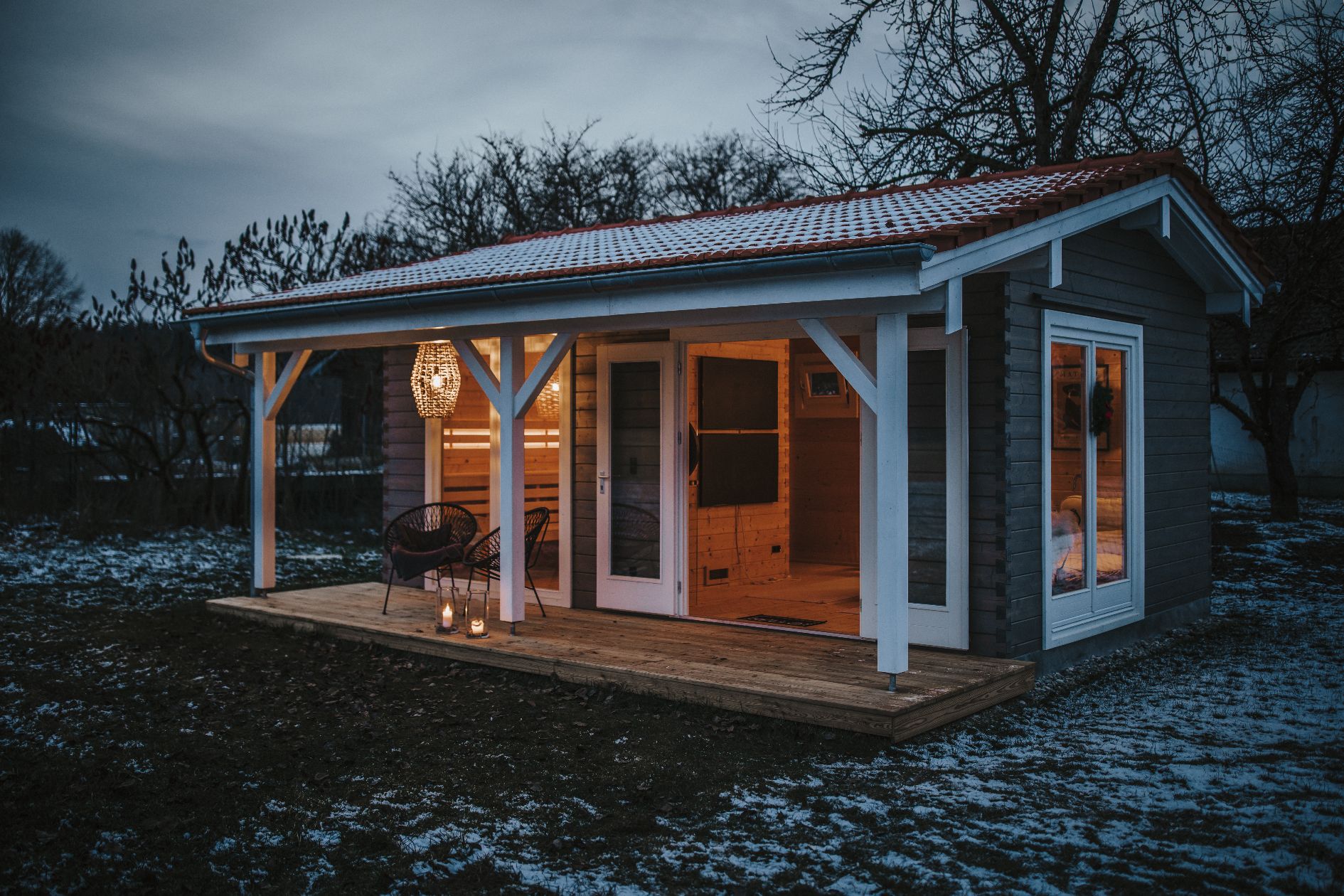 Saunahaus aus Holz mit beleuchteter Terrasse in der Abenddämmerung.