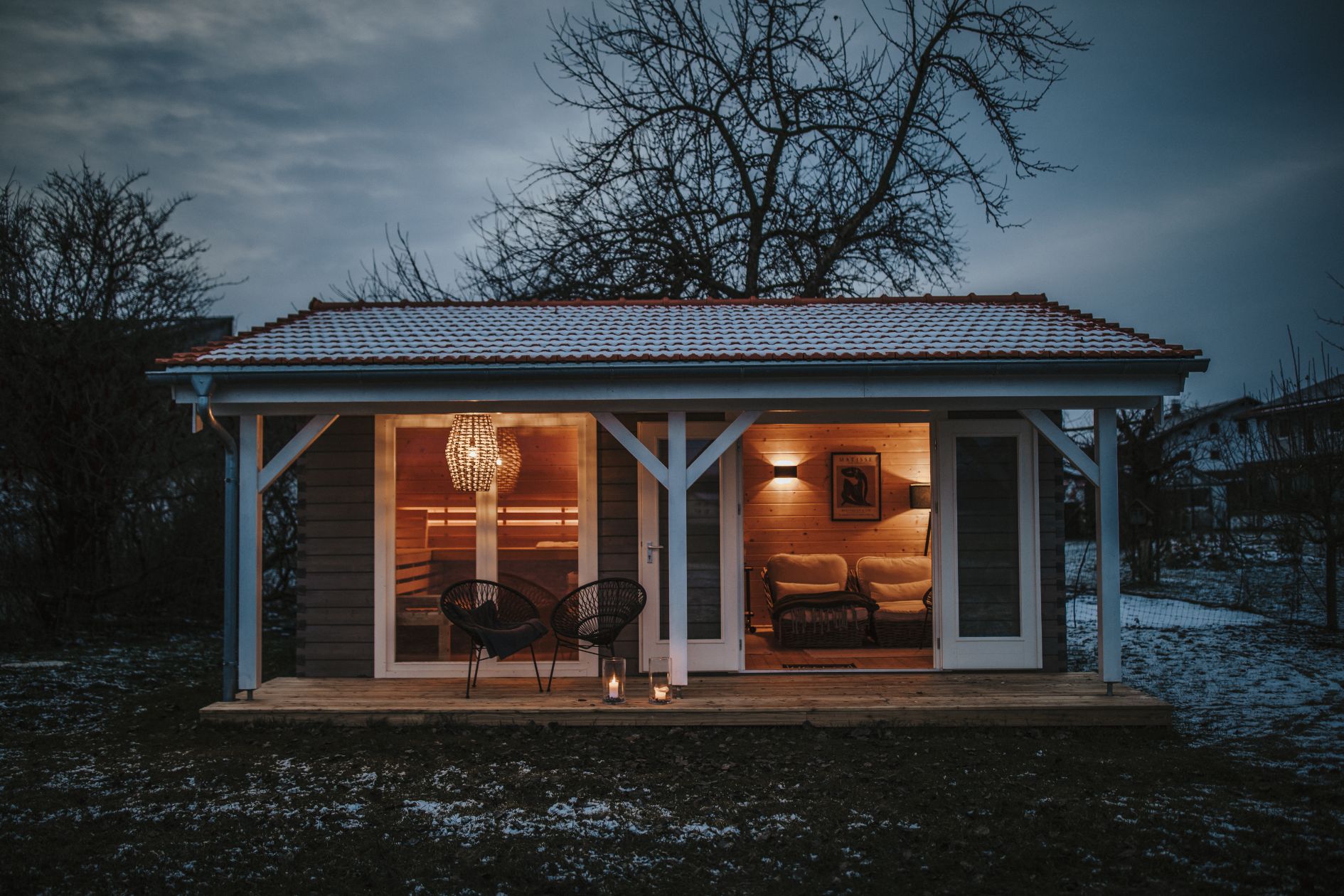 Saunahaus aus Holz mit beleuchteter Terrasse in der Abenddämmerung.