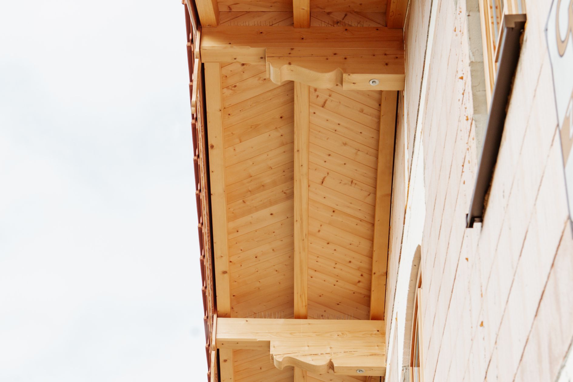 Detailansicht eines Vordachs mit Sichtschalung in Fischgrätoptik und handgefertigter Windbrettverzierung an einem Neubau.